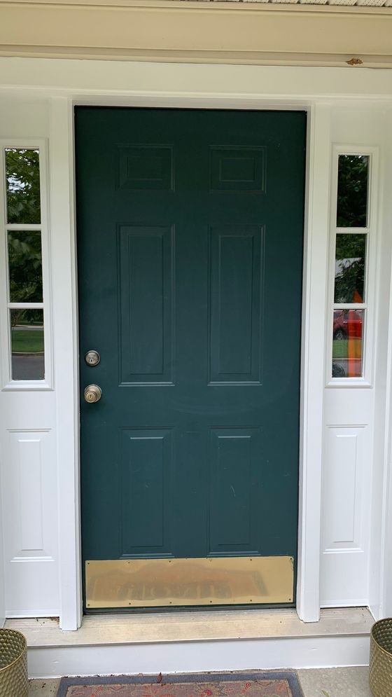 Dark green front door with white trim and sidelights, slightly worn at the bottom.