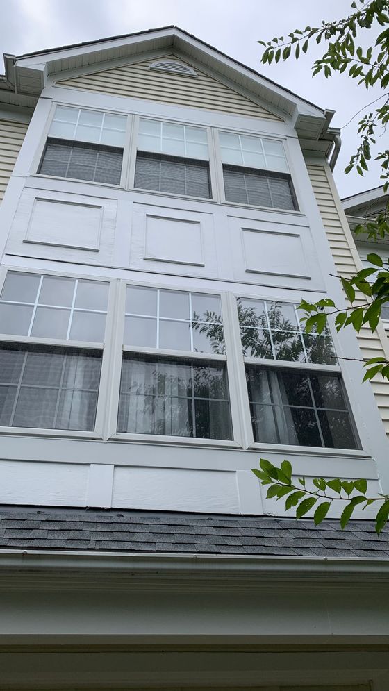 White house exterior with tall windows, gray shingled roof, and tree branches in the foreground