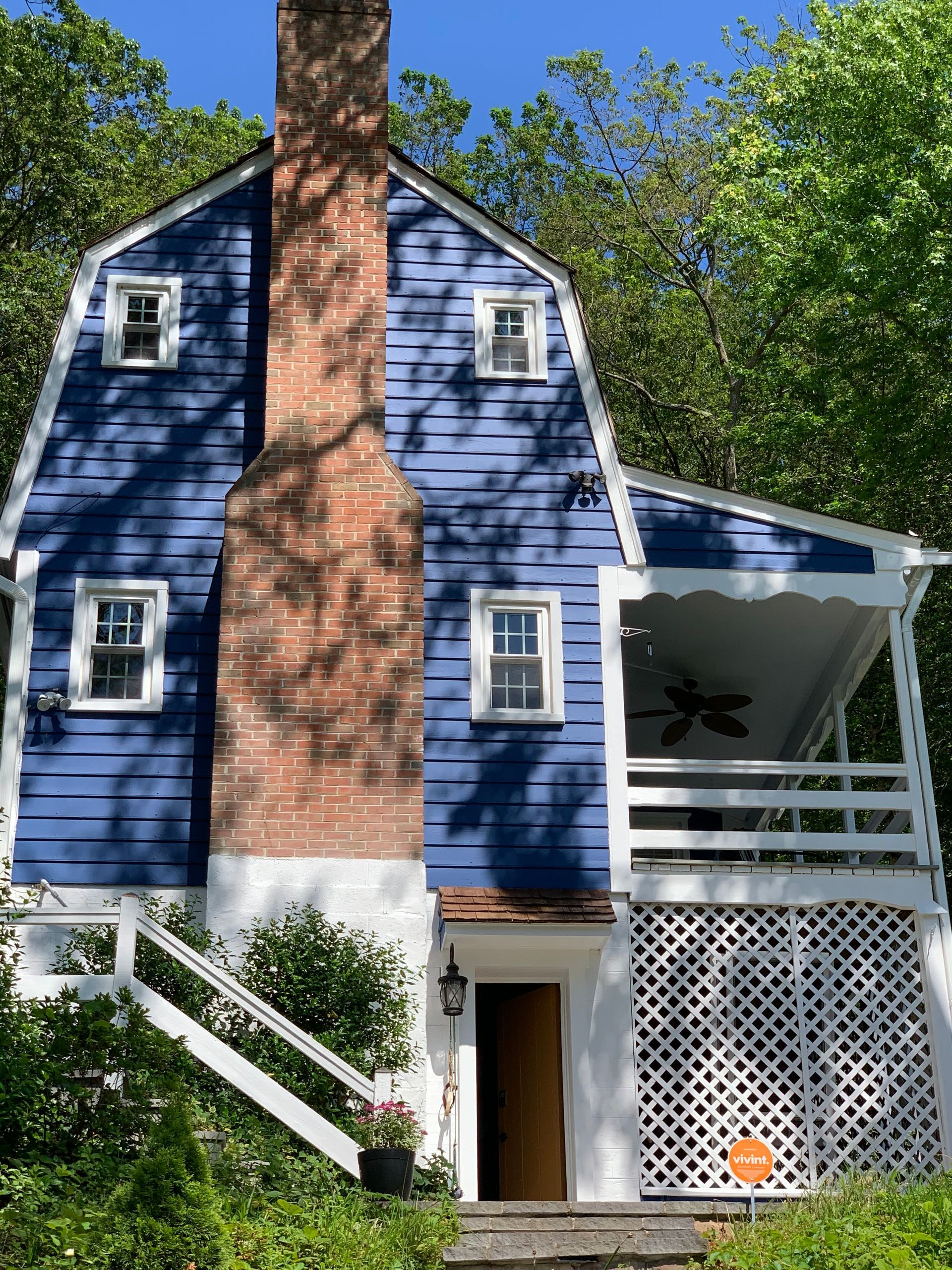 Blue house with a tall brick chimney, white trim, and a covered porch in a wooded setting