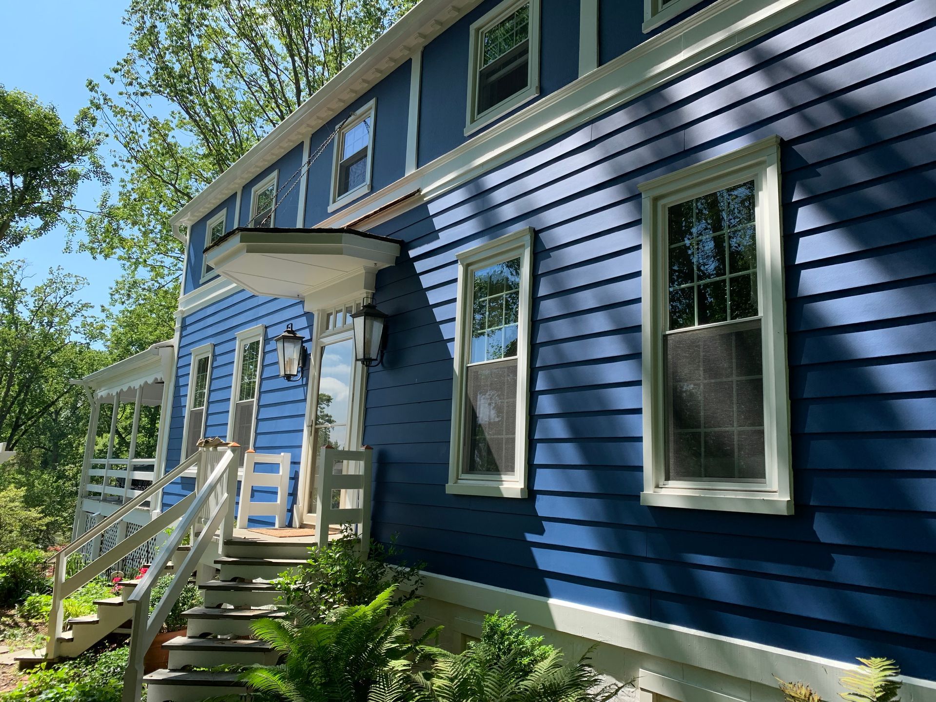 Blue house exterior with white trim, front steps, and a small porch among trees