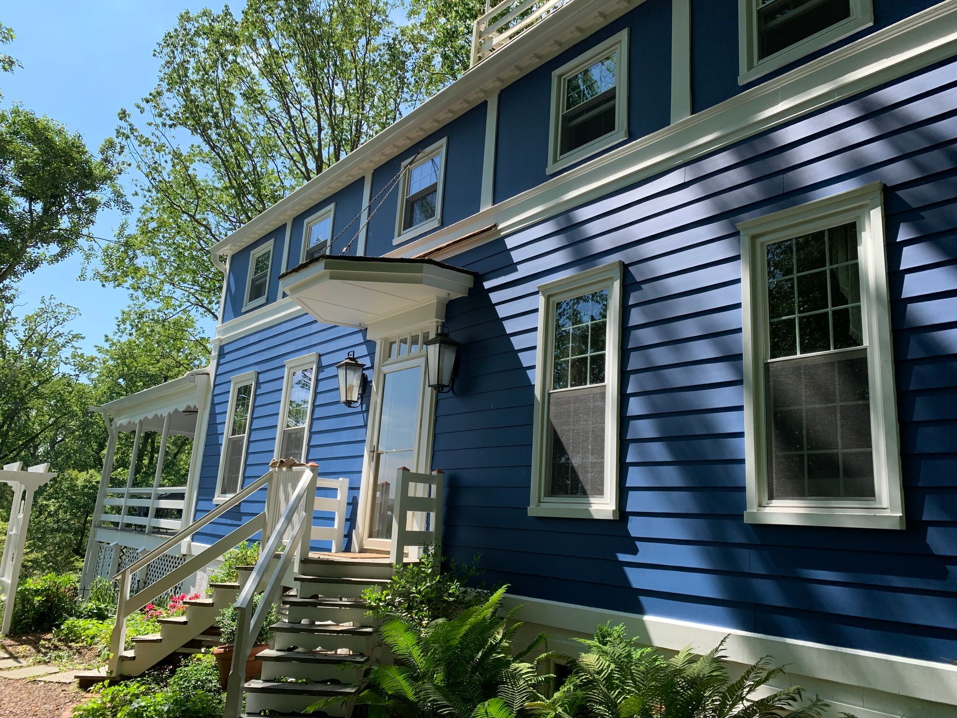 Blue house exterior with white trim, front steps, and dormer windows surrounded by trees