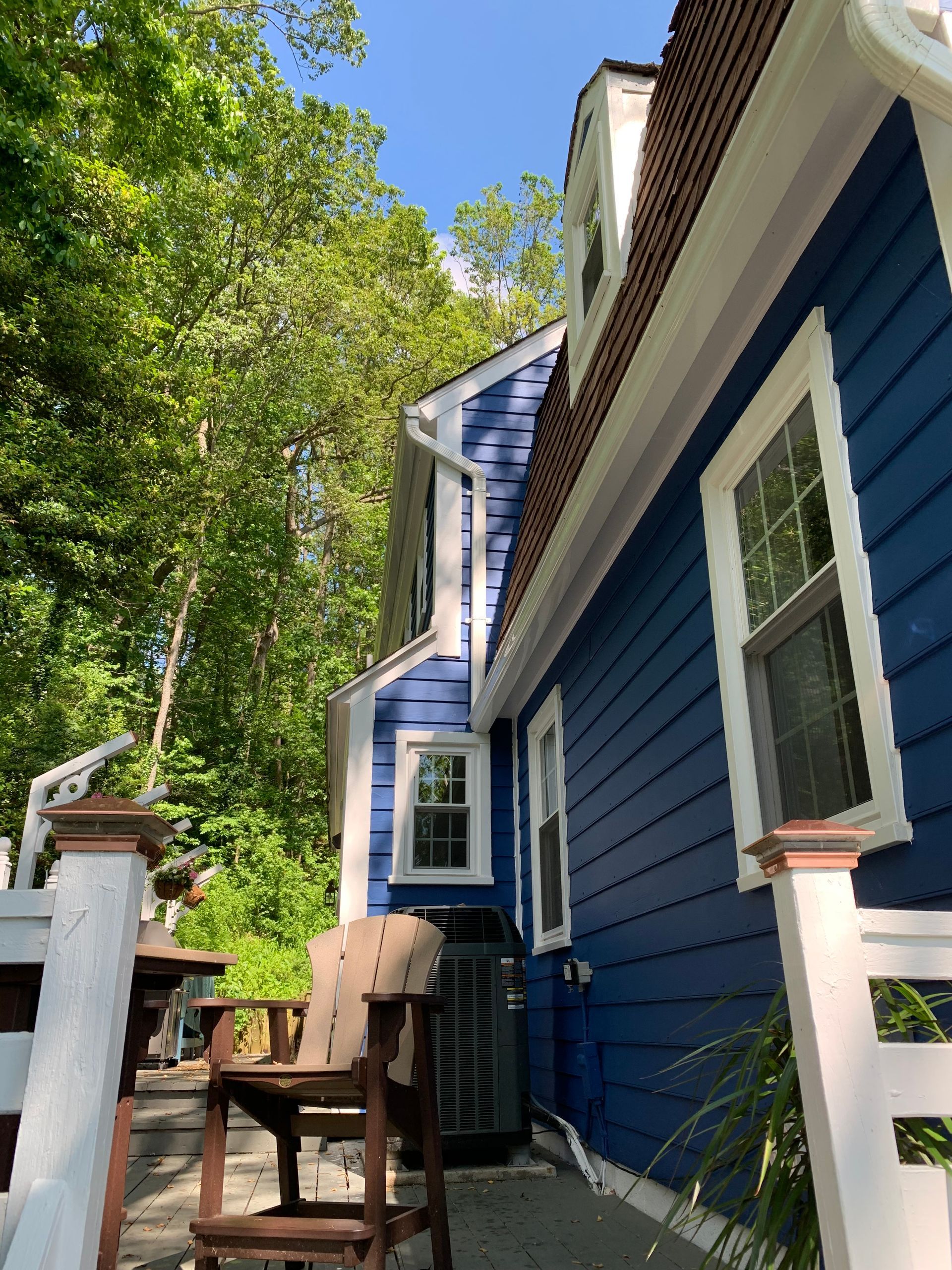 Blue house exterior with white trim, a chair on the porch, and trees in the yard.