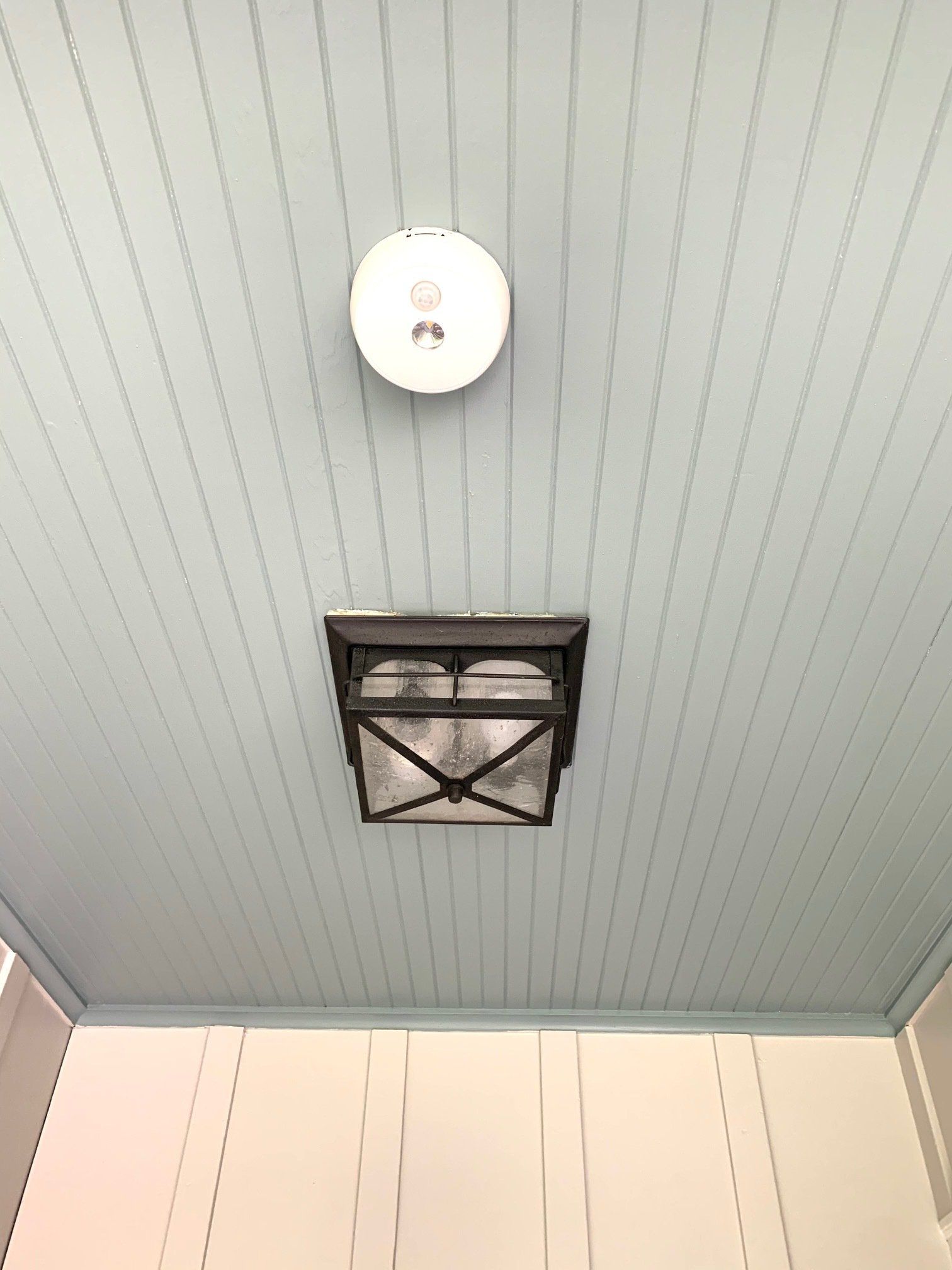 Blue paneled ceiling with a round smoke detector and a black ceiling vent