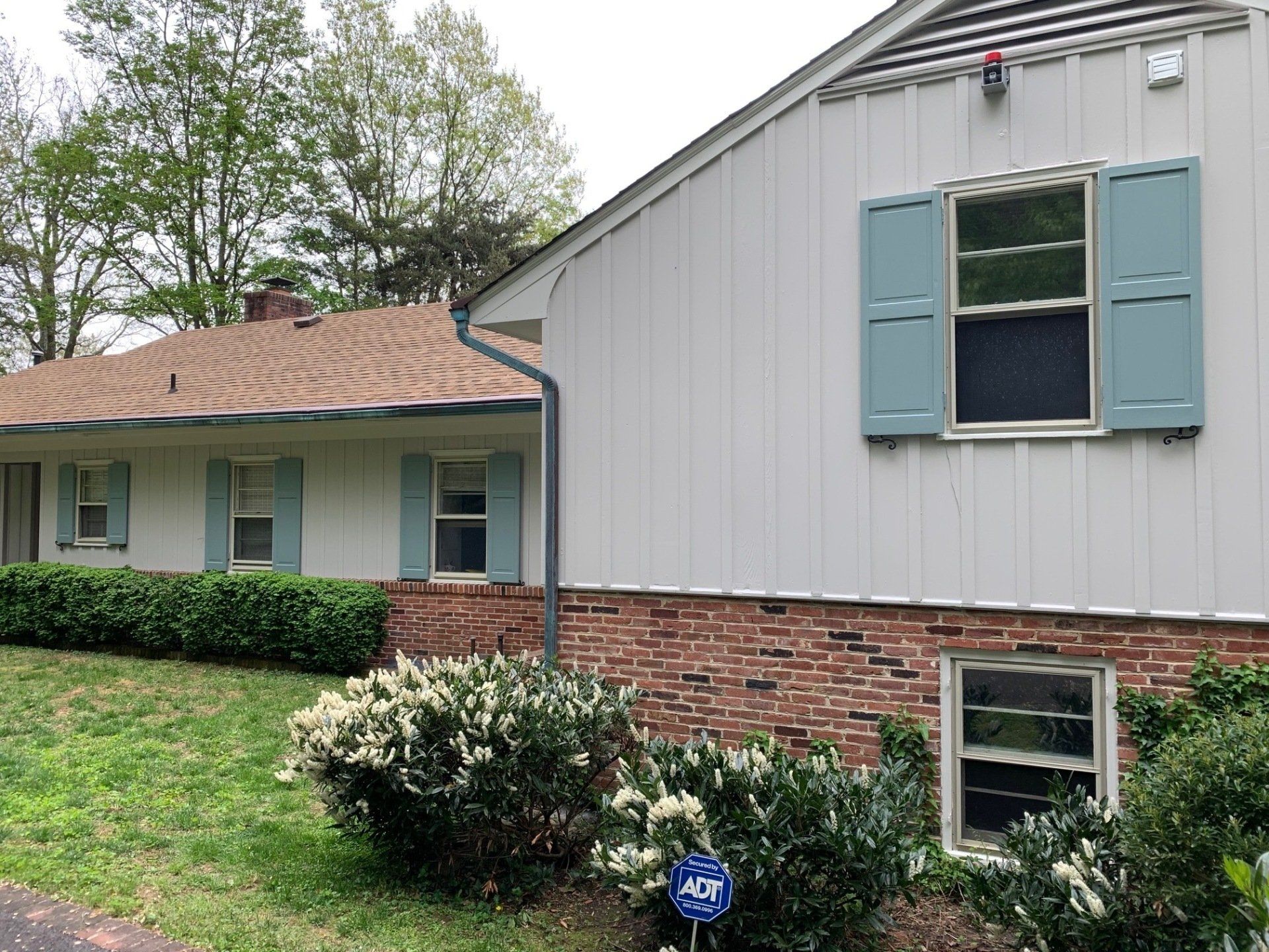 Suburban house exterior with brick and gray siding, blue shutters, and trimmed bushes in front of a lawn