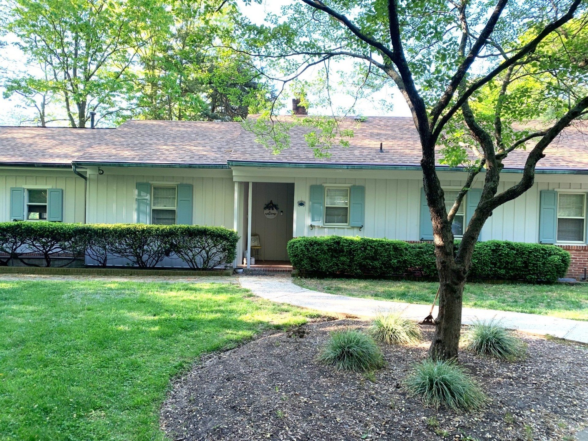 Single-story house with light green exterior, front porch, manicured lawn, and trees in front yard