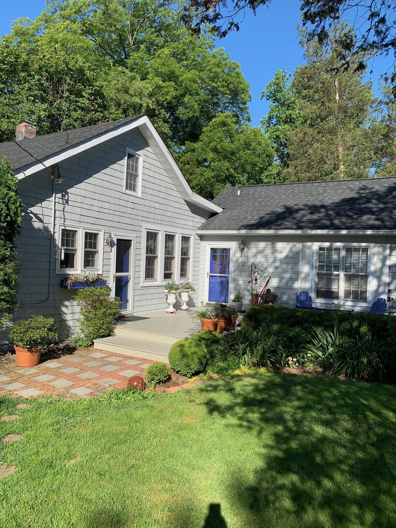 Gray stone house with blue front door, steps, and a sunny green lawn framed by trees