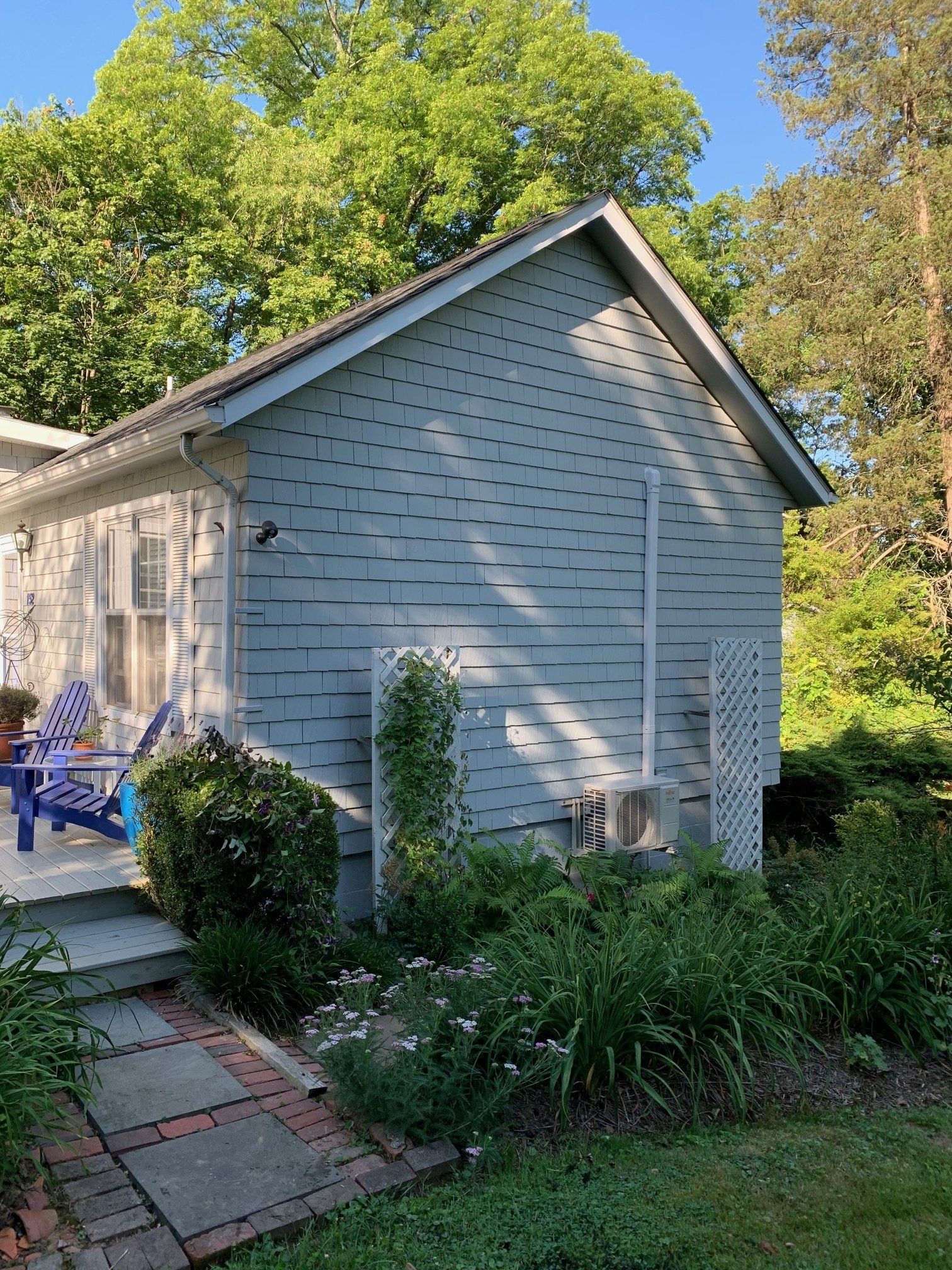 White-sided house with blue trim, garden plants, and a brick path in a sunny yard