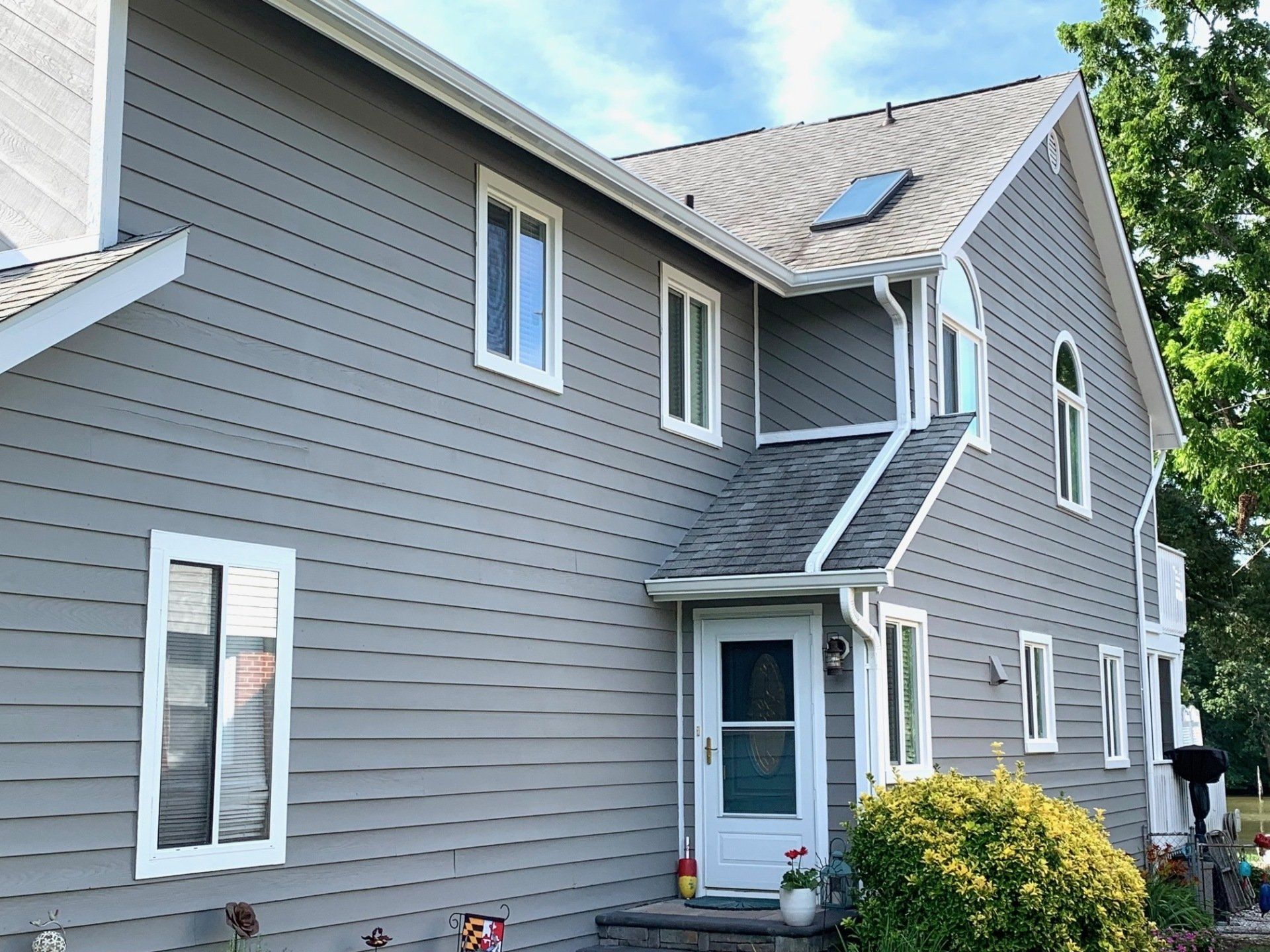 Gray two-story house with white trim, several windows, and a small covered entryway under a sloped roof.