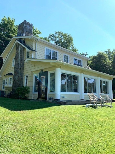 Yellow house with white trim and a sunroom on a grassy lawn under a blue sky