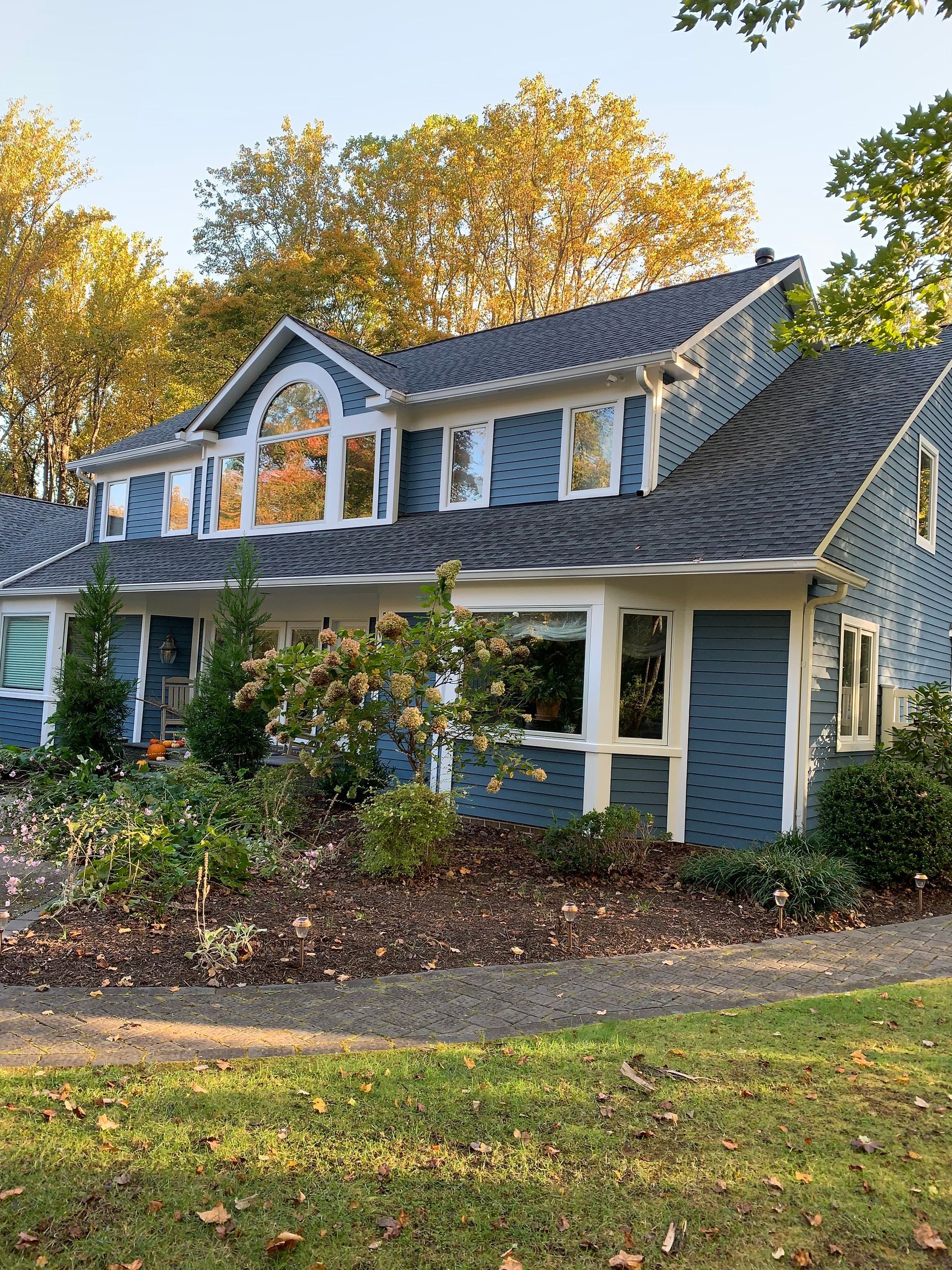 Blue house with white trim, dormer windows, and a landscaped front yard in autumn light