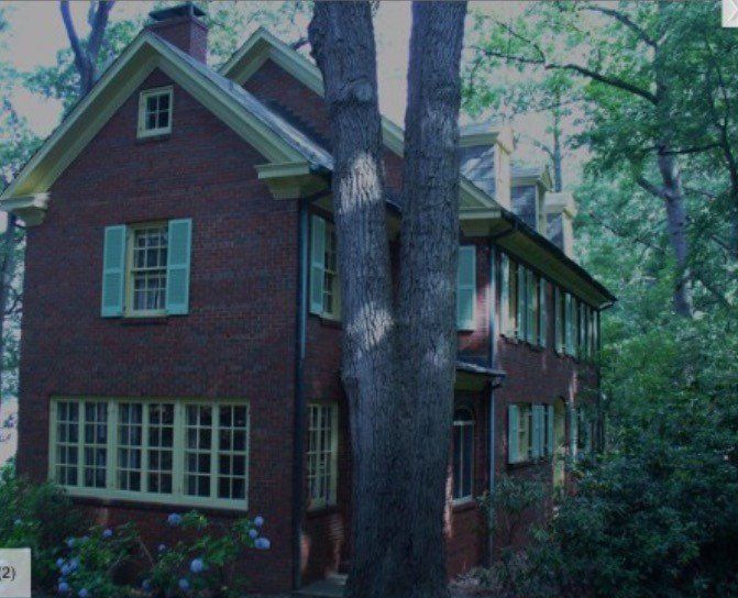 Brick house with white-trimmed windows and tall trees in a wooded yard