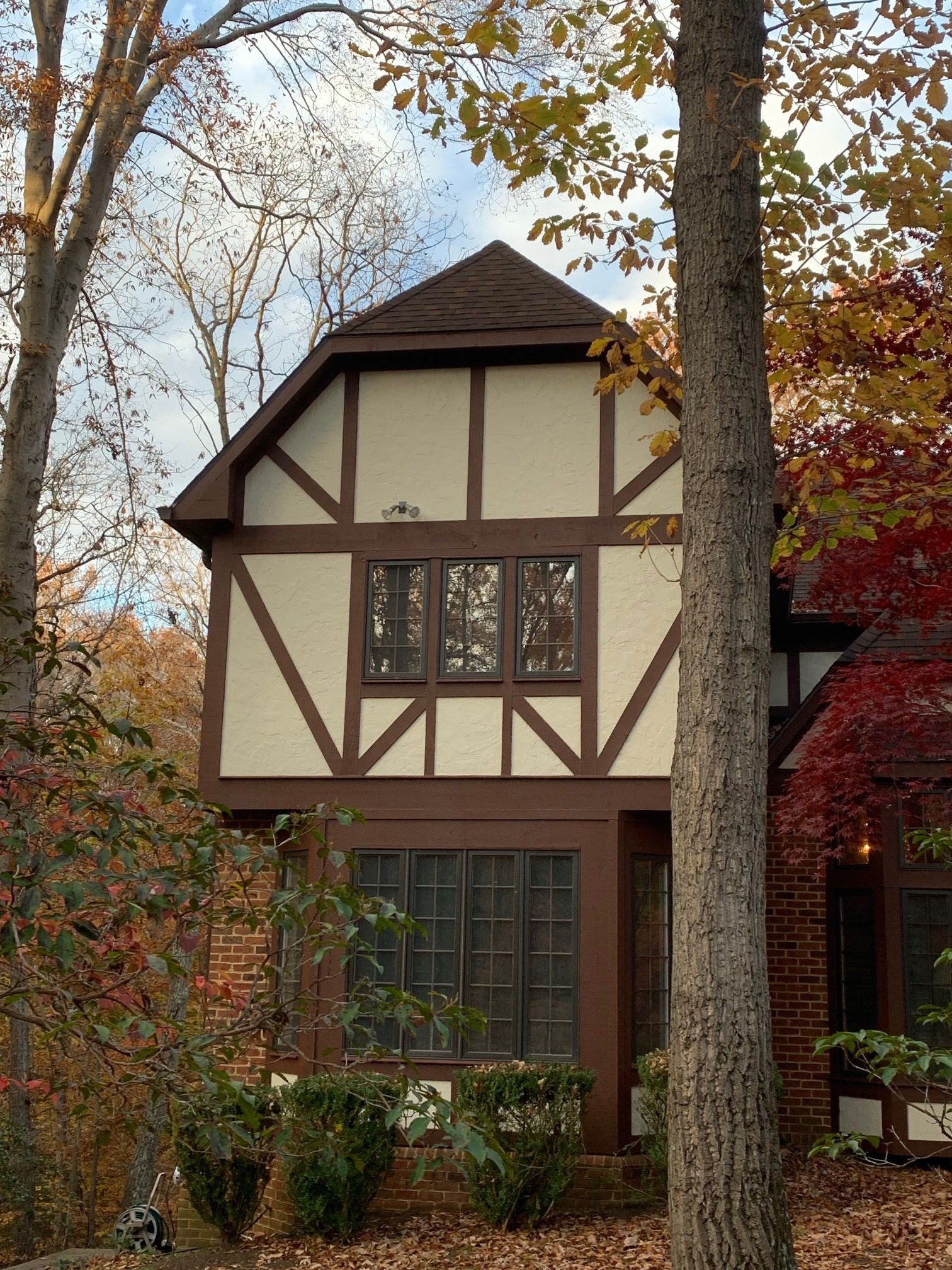 Tudor-style house with beige and brown timber framing, framed by autumn trees and foliage