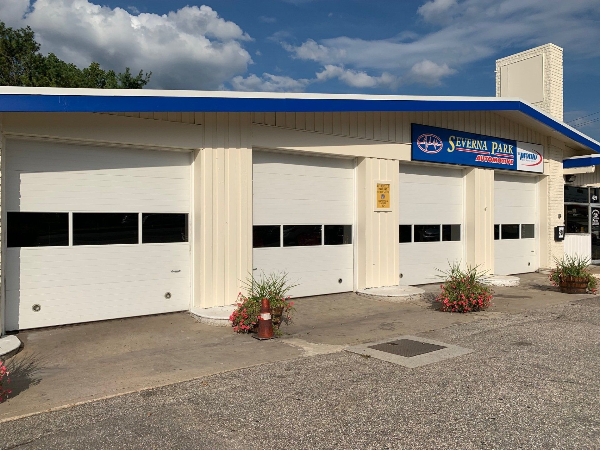 White auto shop with blue roof trim, garage doors, and a sign under a cloudy sky