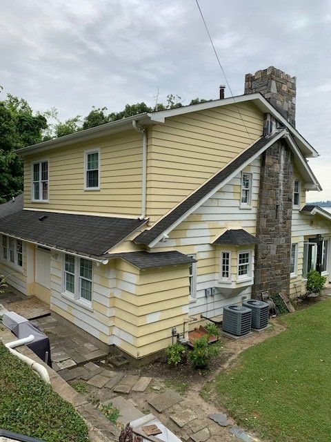 Yellow two-story house with stone chimney, gray roof, and stone walkway in a grassy yard