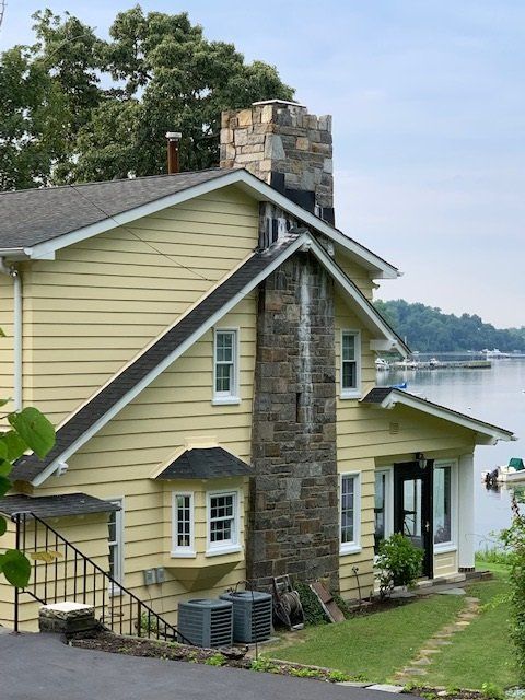 Stone house with yellow siding and chimney on a grassy lakeside hill