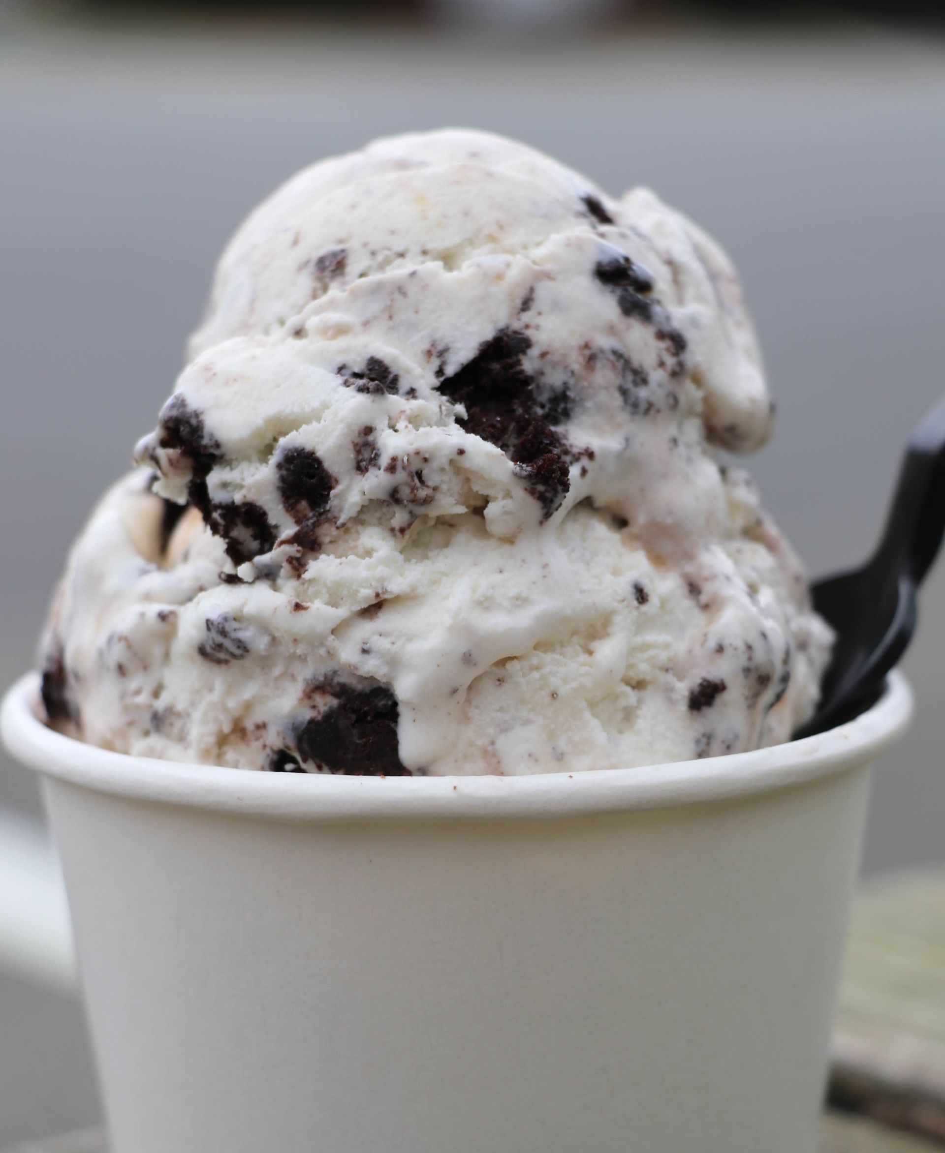 A scoop of cookies and cream ice cream in a white paper cup with a black spoon.