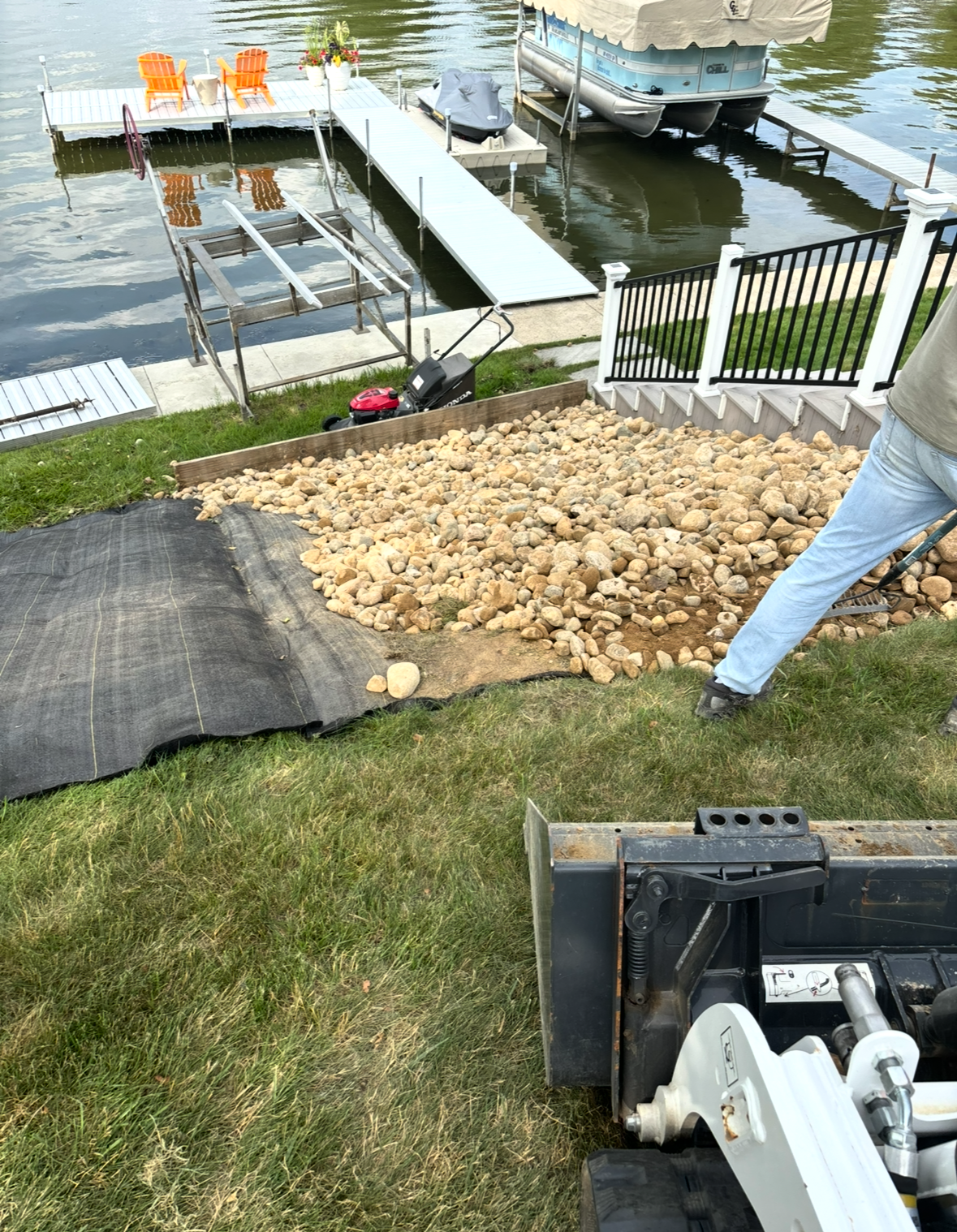 Backyard lakeside dock with rocks, white ramp, and a person standing near the shore