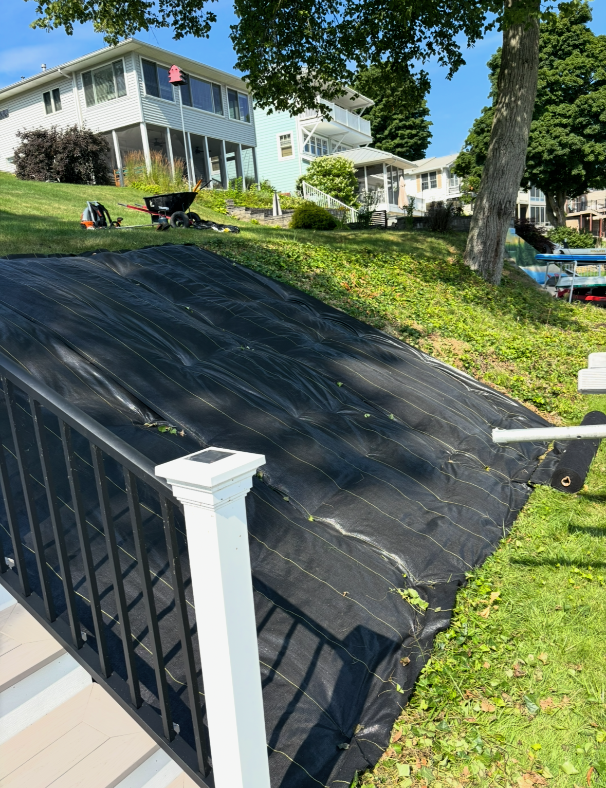 Sloped black roof with white railing overlooking a lakeside yard and house on a sunny day