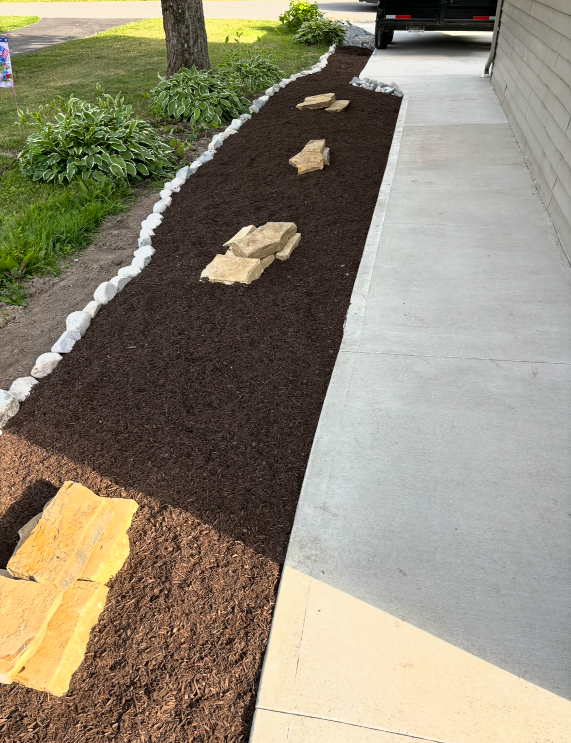 Fresh mulch border along a driveway with stepping stones beside a concrete walkway