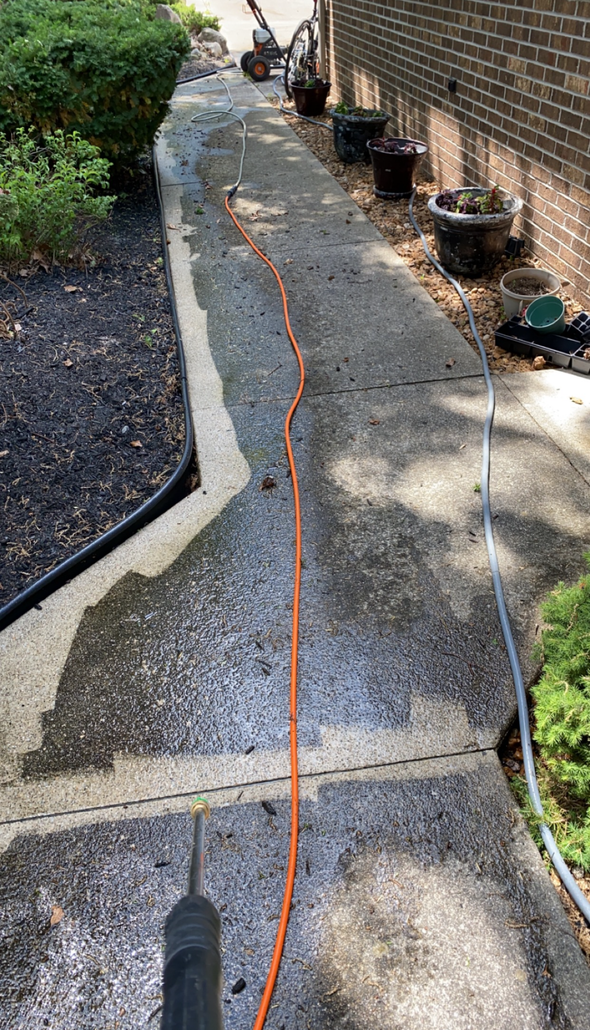 Narrow concrete walkway beside a brick wall, with an orange extension cord running along it.
