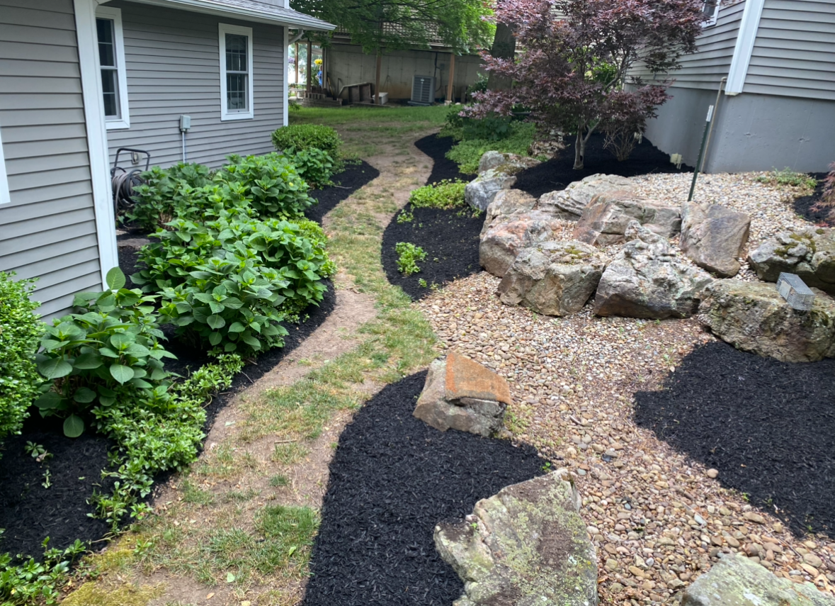 Curved mulched garden path between house siding and stone landscaping with green shrubs and trees