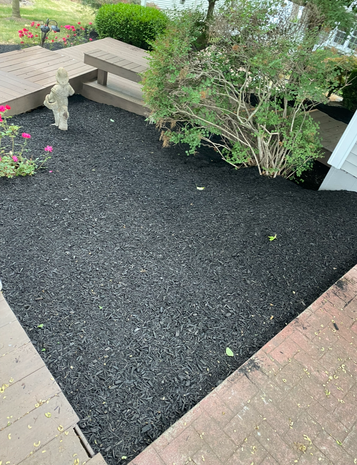 Small garden bed with black gravel, stone bench, shrubs, and brick paving around it