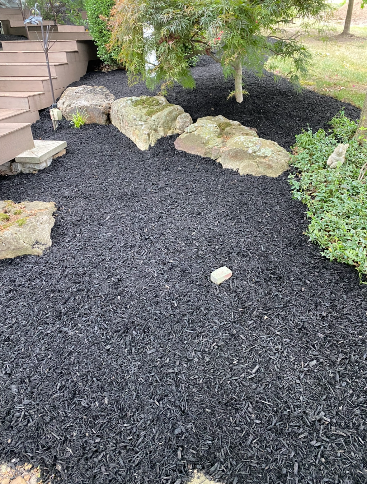Rock-lined garden bed with black mulch and stepping stones beside a house