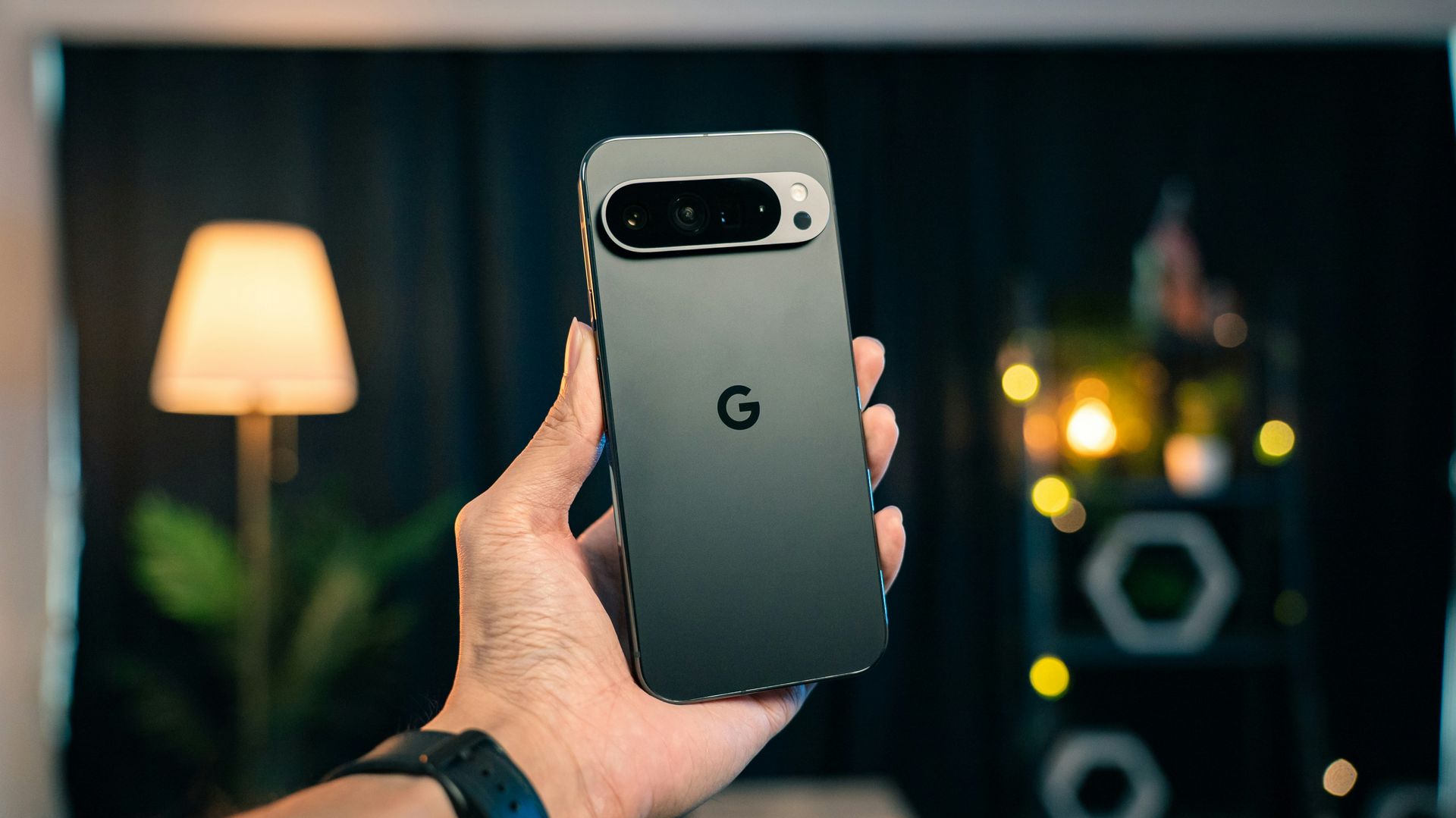 Hand holding a black Google Pixel phone with dual rear cameras against a blurred indoor background