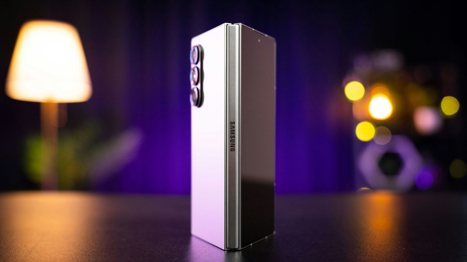Silver smartphone standing upright on a table with blurred purple and warm lights in the background