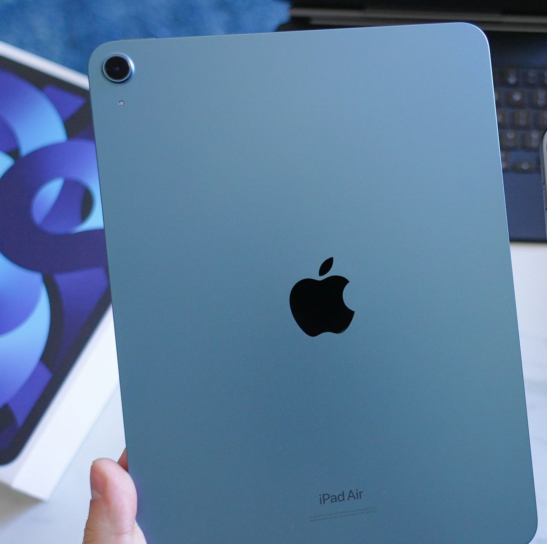 Back of a blue iPad Air with centered Apple logo, held in a hand