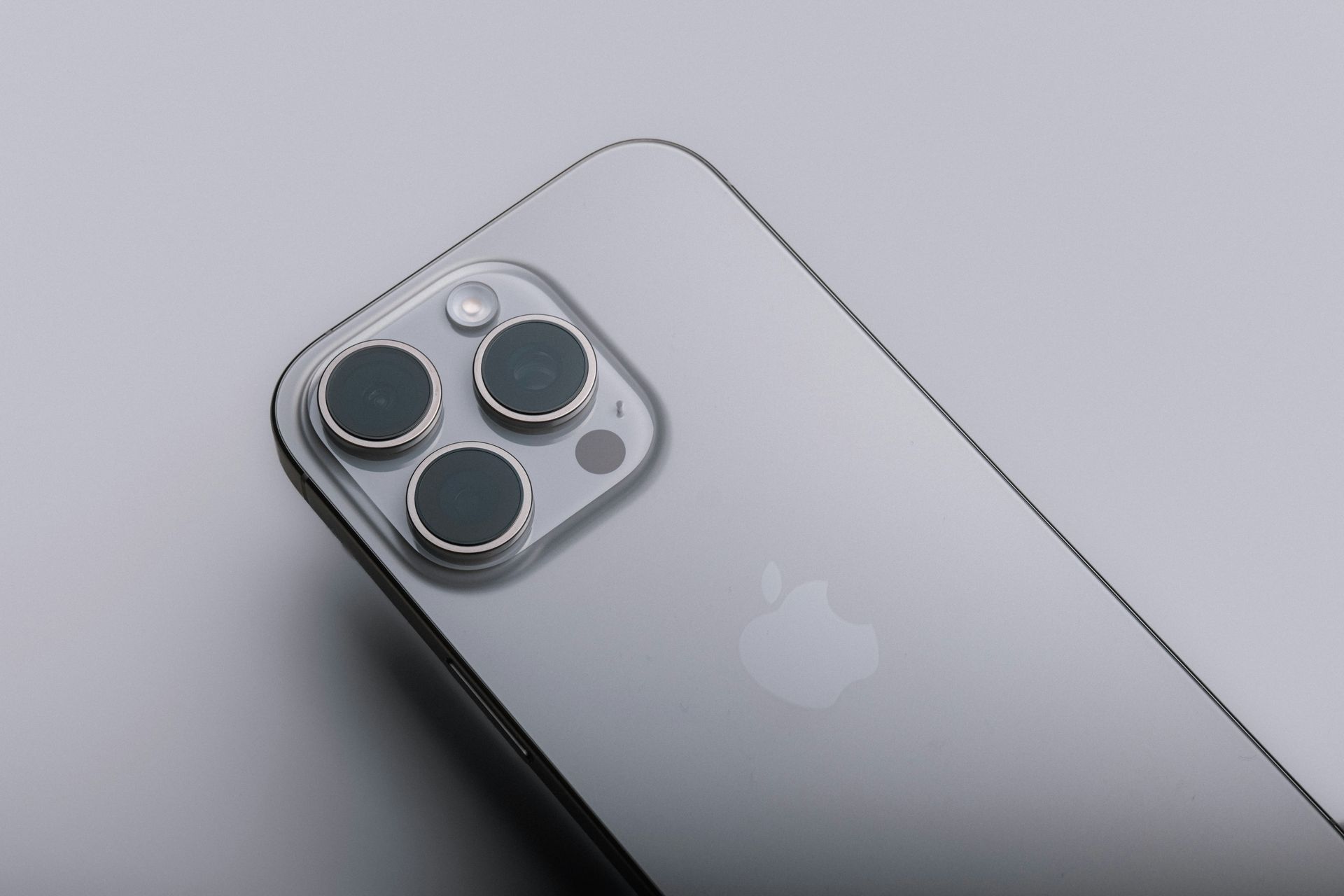 Silver smartphone with triple rear cameras on a light gray background