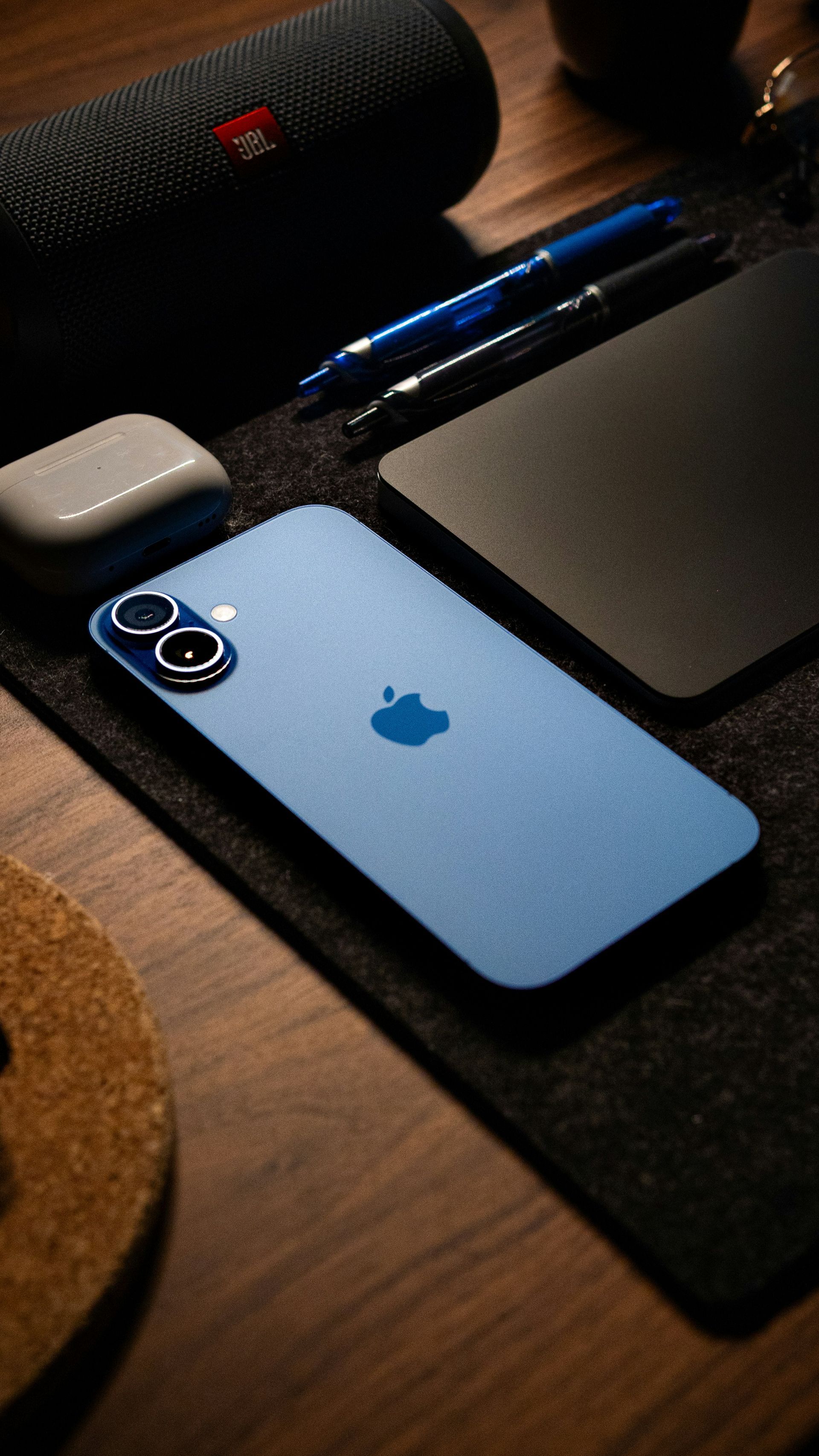 Blue iPhone lying on a desk beside a pen, mouse, and black desk mat.