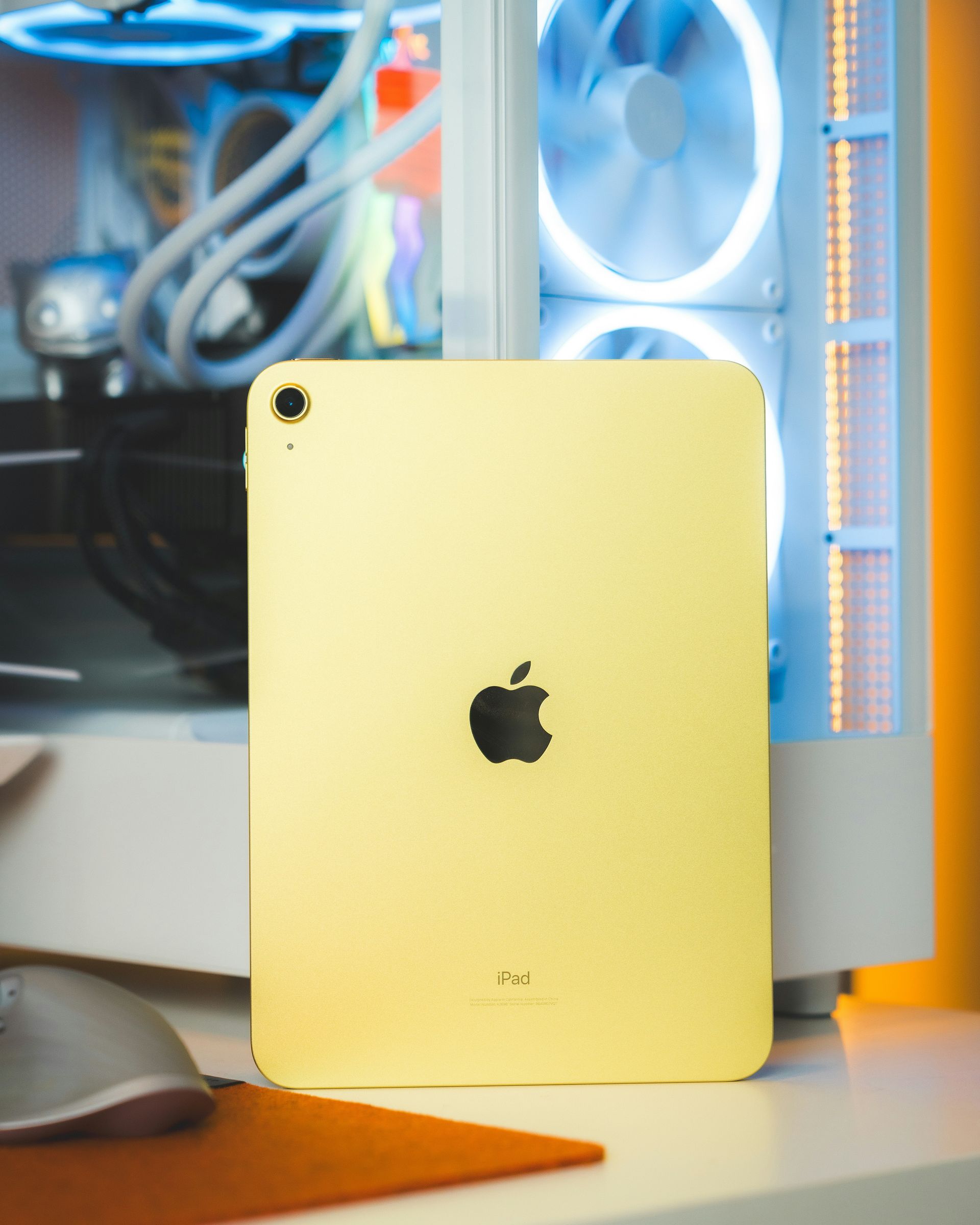 Gold iPad standing on a desk in front of a PC tower with blue-lit fans