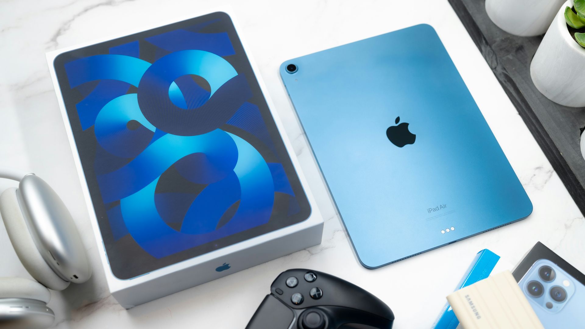 Blue iPad box and blue iPad on a white desk with a game controller nearby