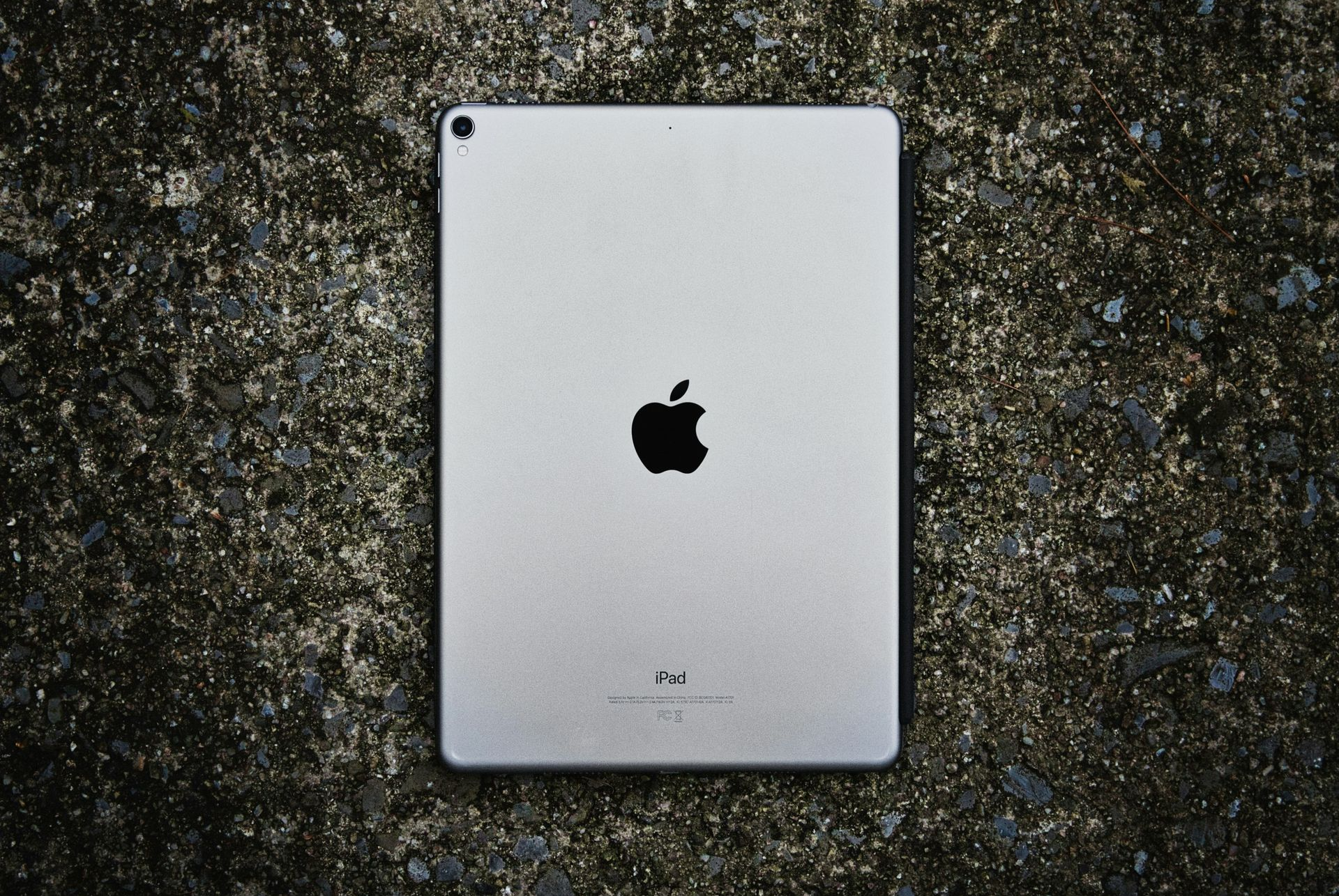 Silver Apple tablet lying on dark wet pavement, viewed from above.