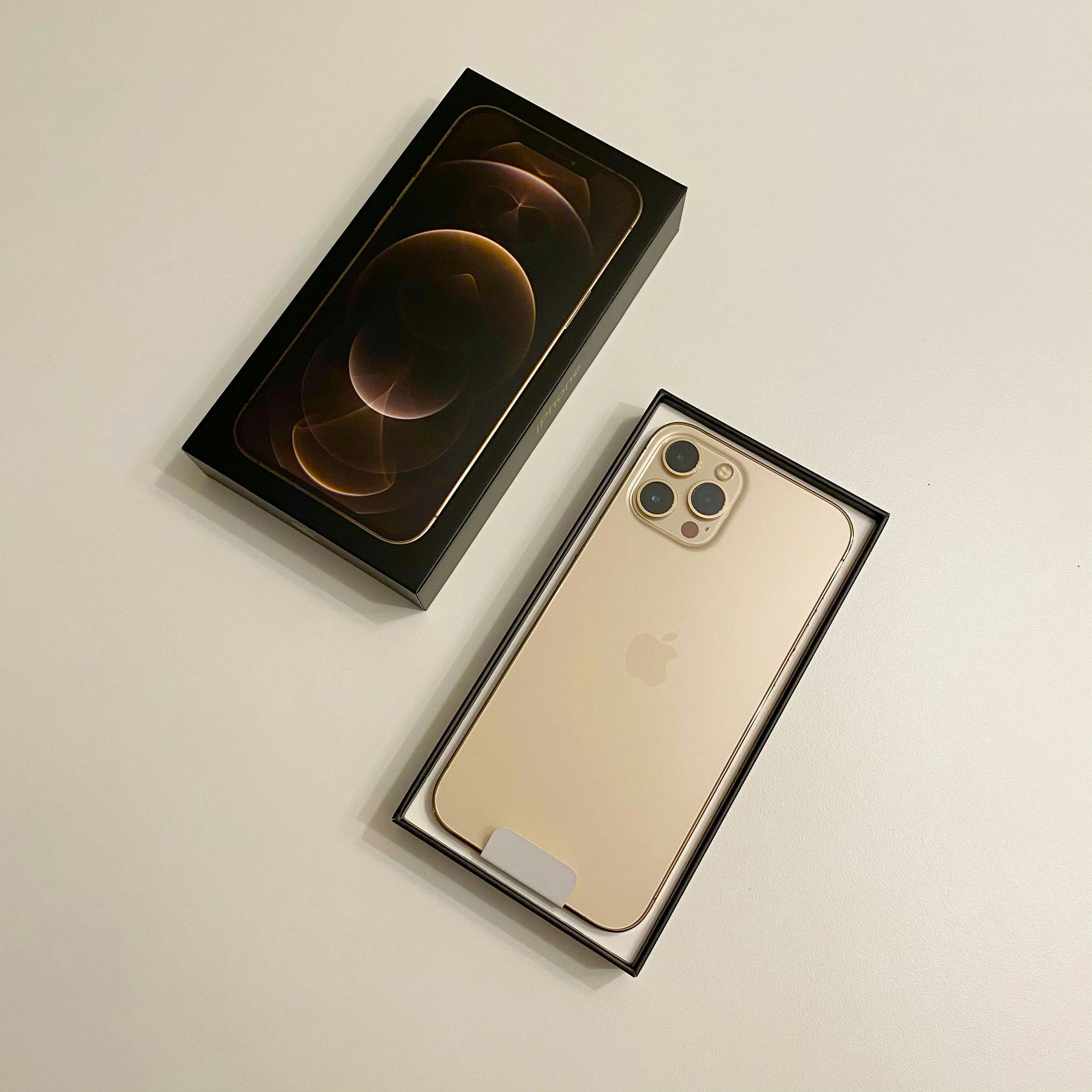 Two iPhones in open boxes on a light surface, one gold phone shown from the back and one box lid above.