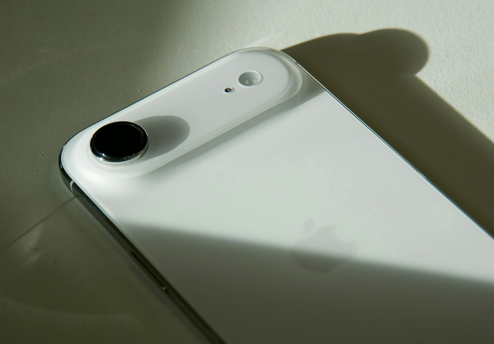 White smartphone back with a single black camera lens in soft light and shadow