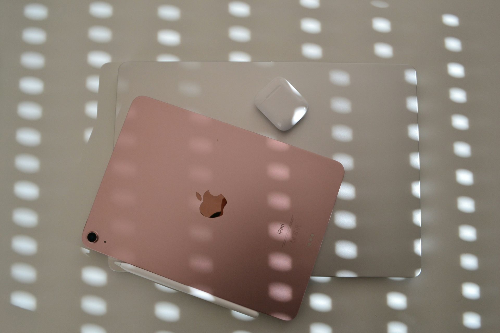 Rose gold MacBook with a white AirPods case on a perforated surface.