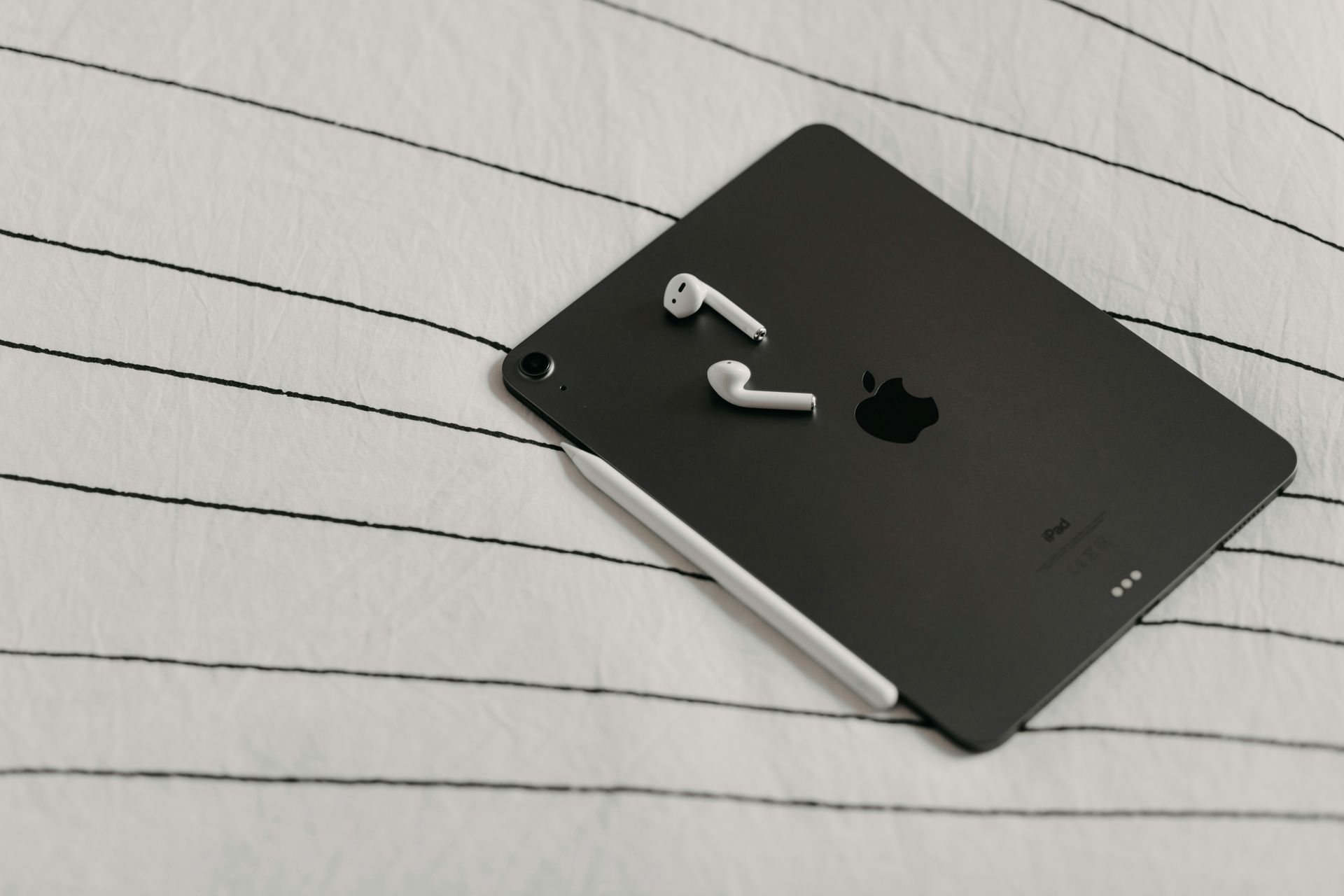 Black iPad with white AirPods on a lined notebook page
