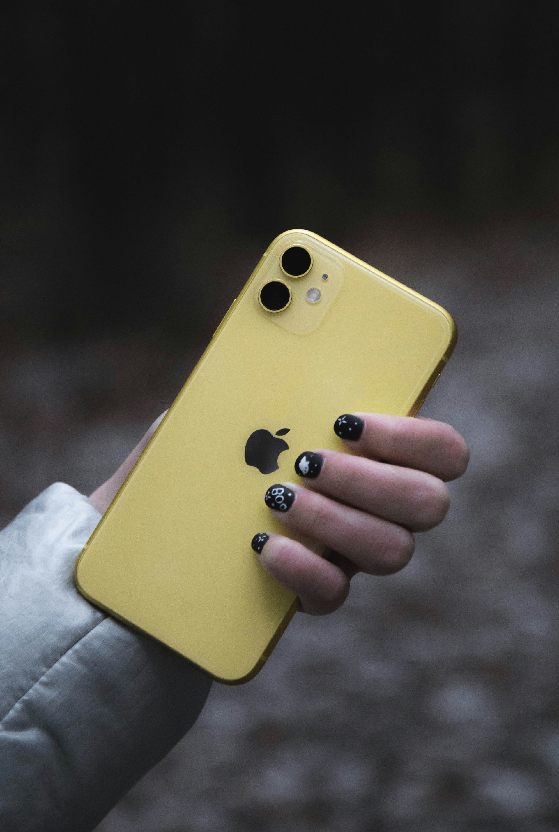 Hand holding a yellow iPhone in a blurred outdoor setting