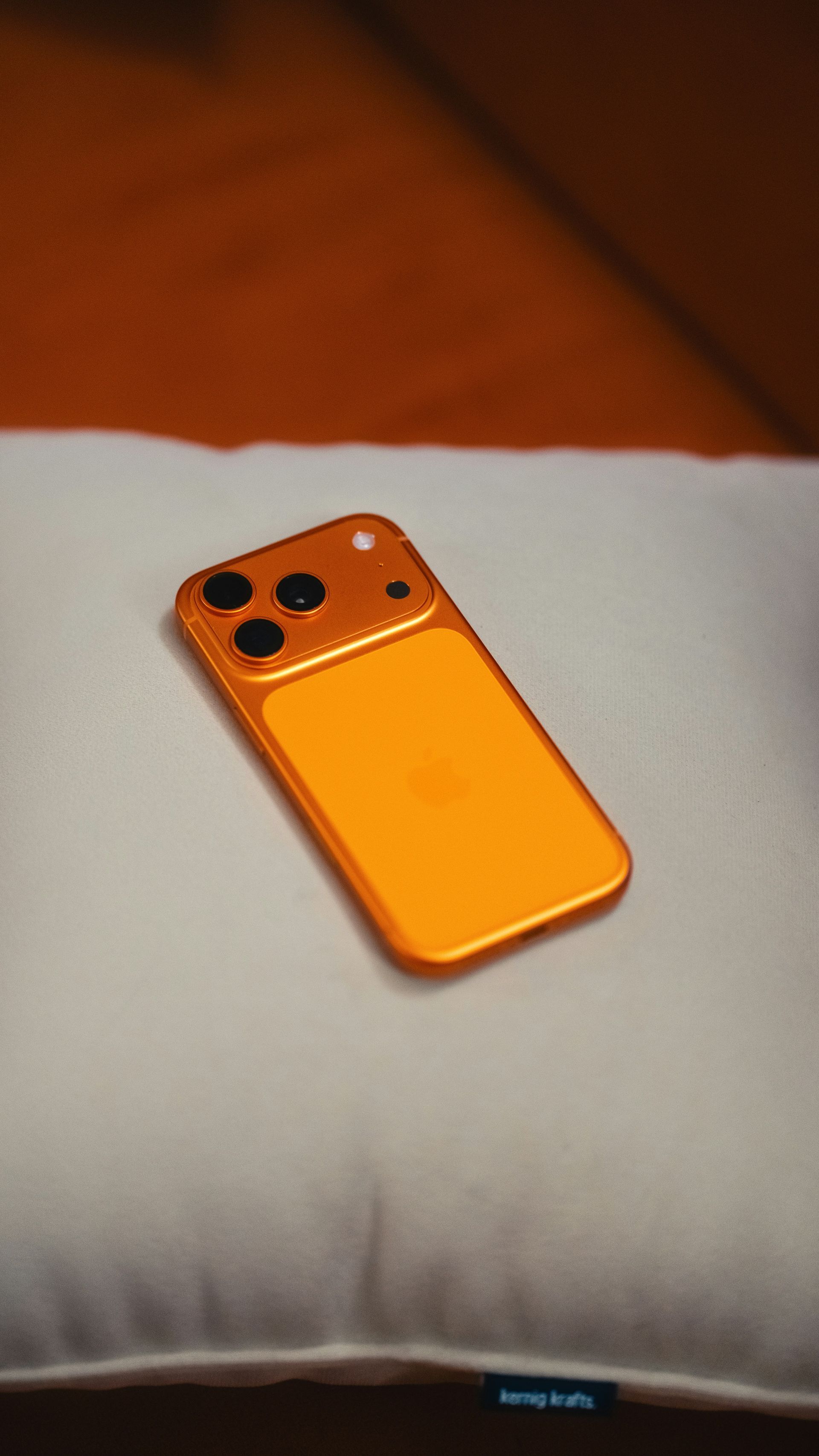 Orange smartphone lying on a white cushion.