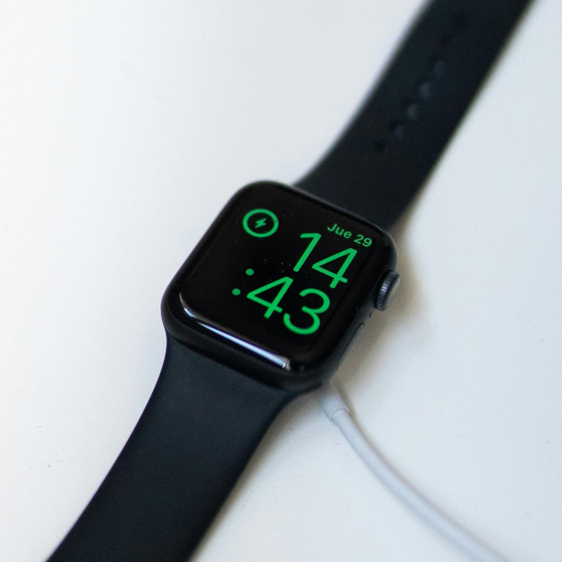 Black smartwatch on a white surface showing 1:43 in green digits
