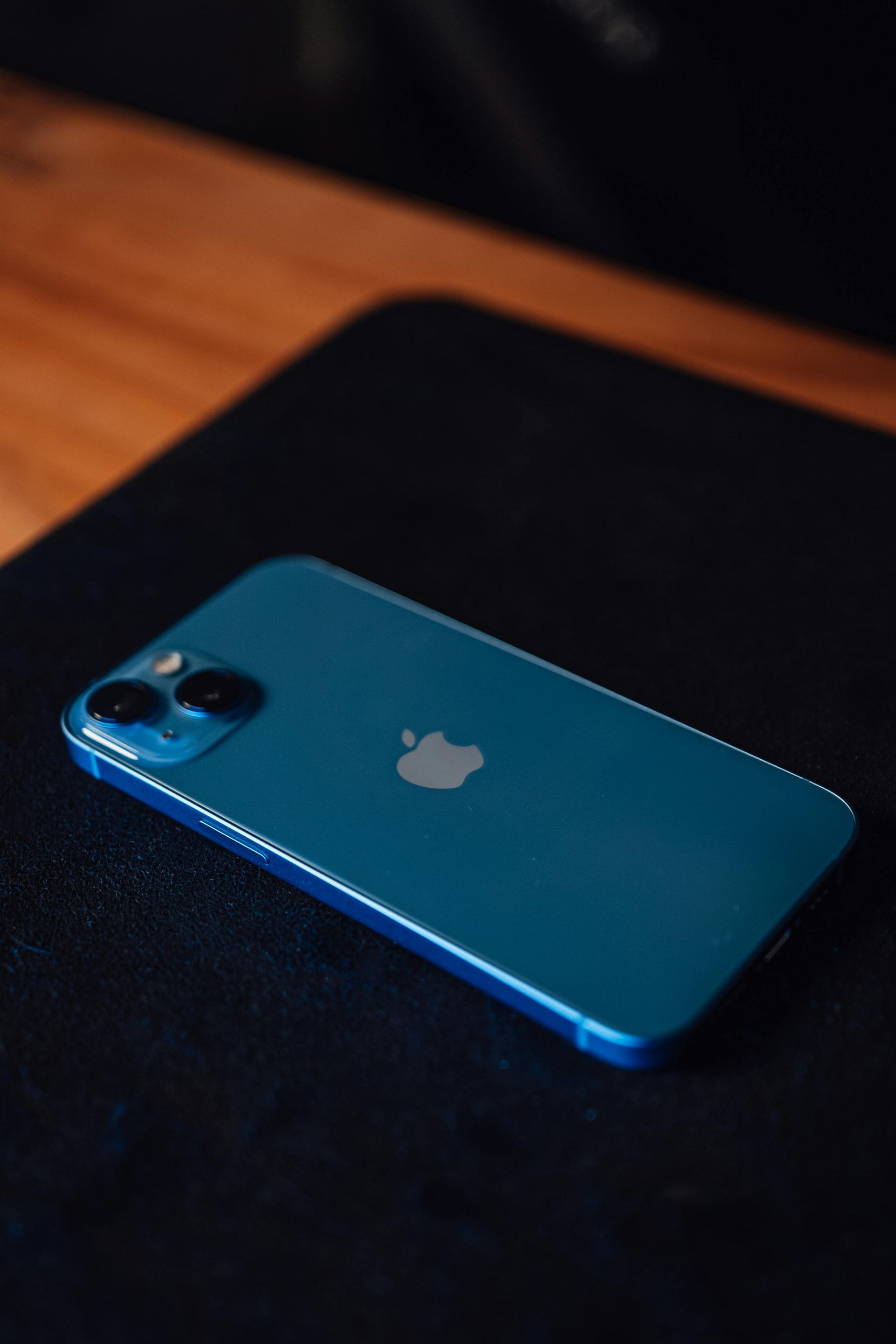 Blue iPhone lying on a black laptop, lit by warm ambient light.
