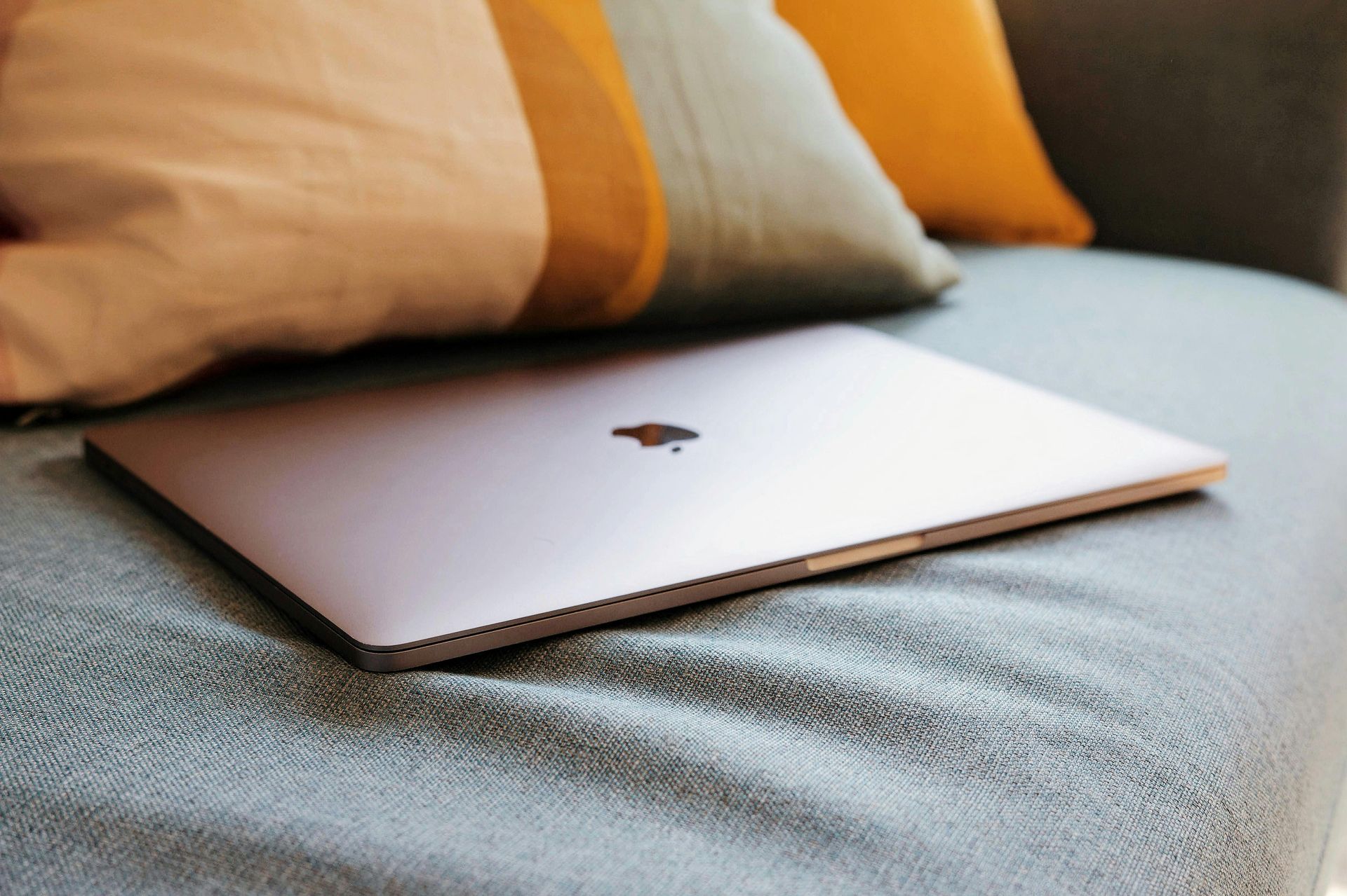 Closed silver laptop on a bed with beige and orange pillows nearby