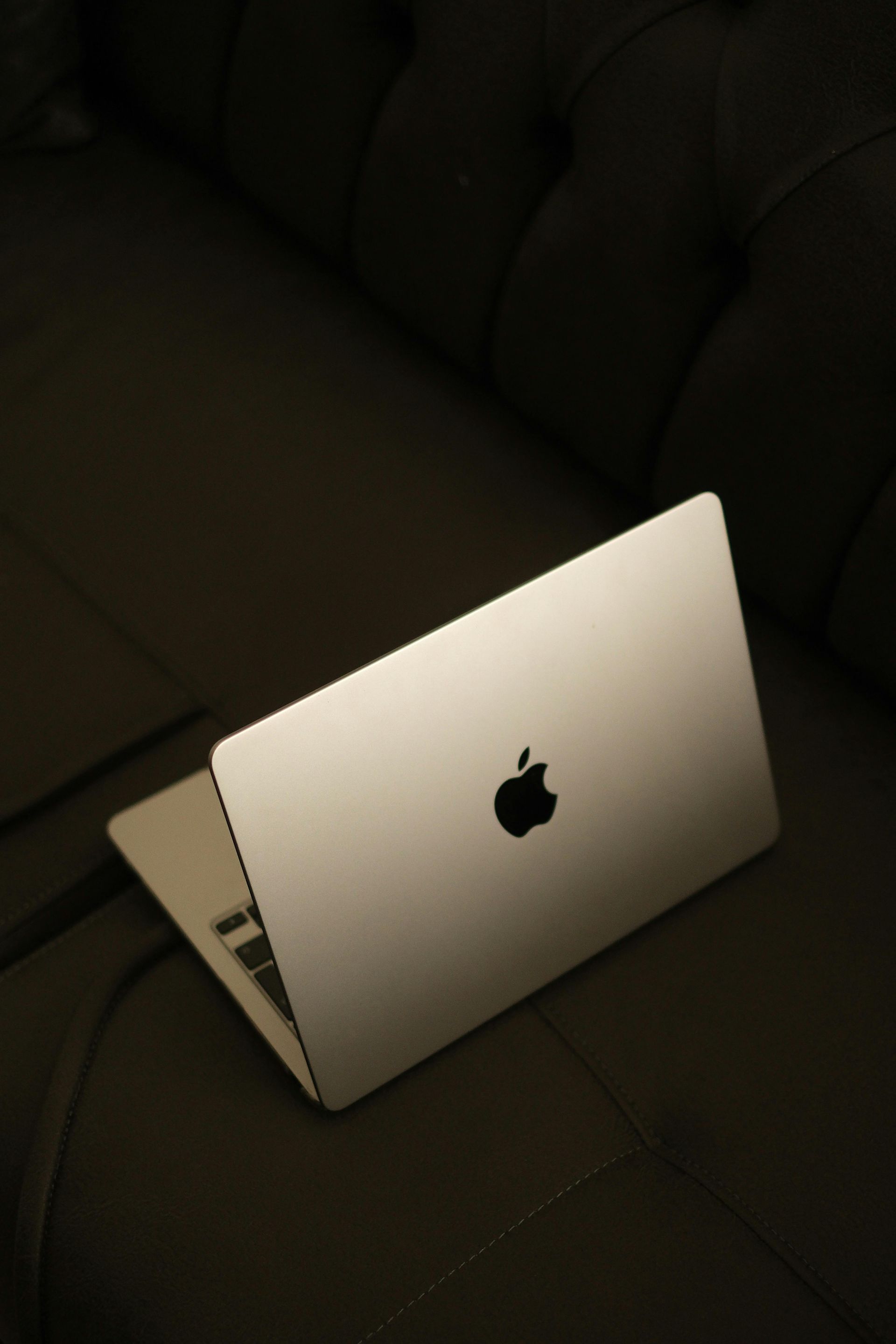 Apple laptop open on a dark couch, lit by warm light.