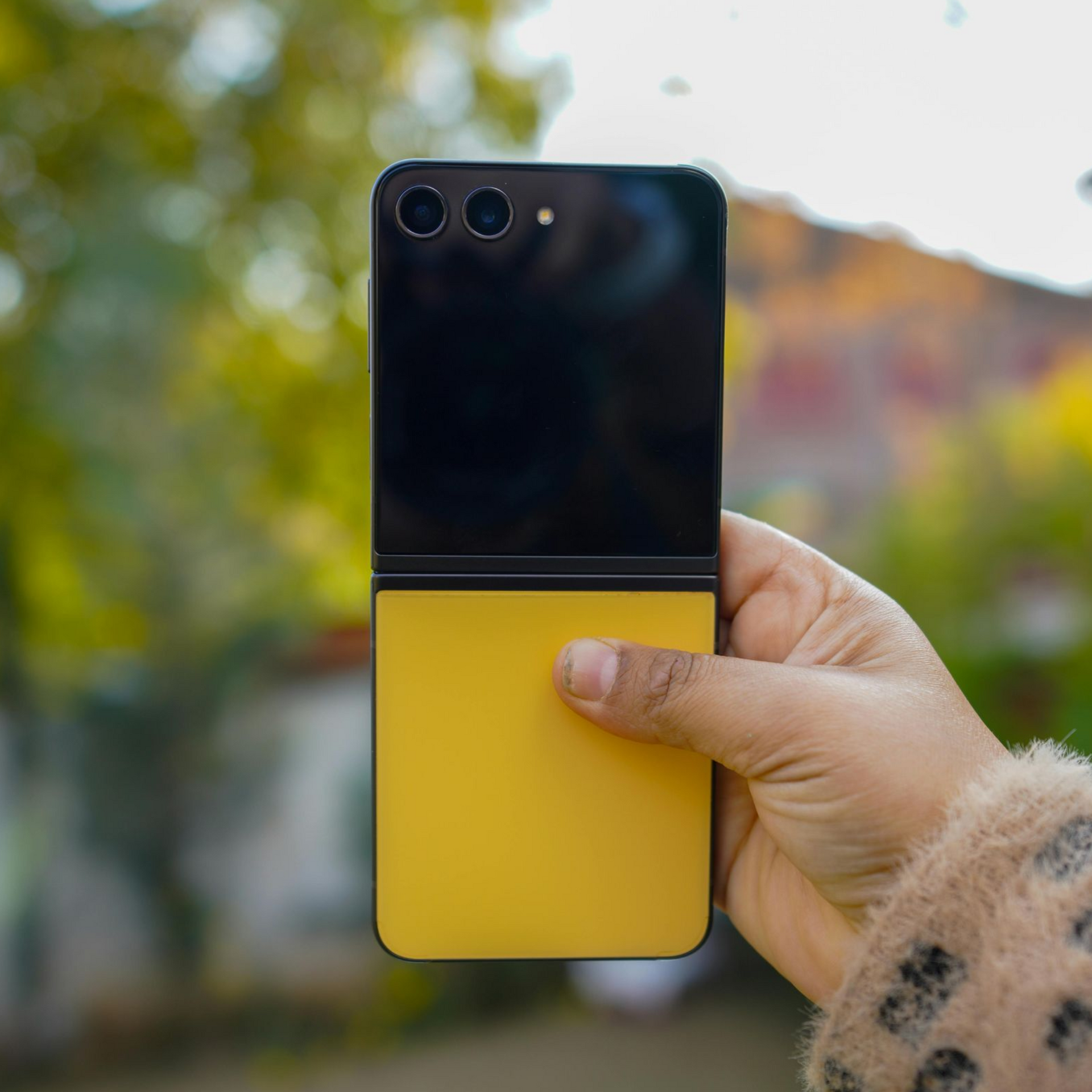 Hand holding a black-and-yellow foldable phone outdoors with blurred trees in the background