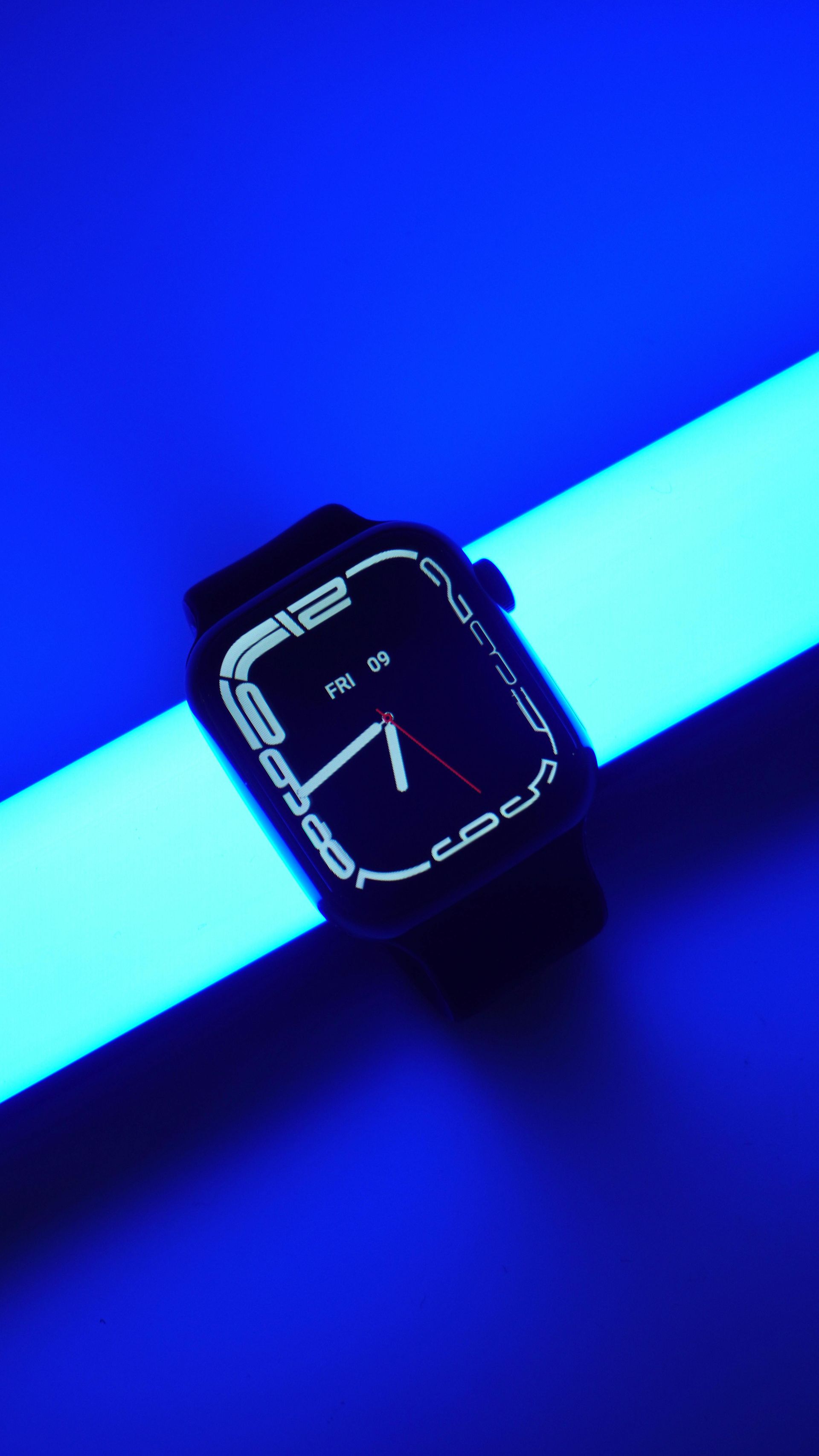 Black smartwatch with white analog display glowing on a blue-lit surface.
