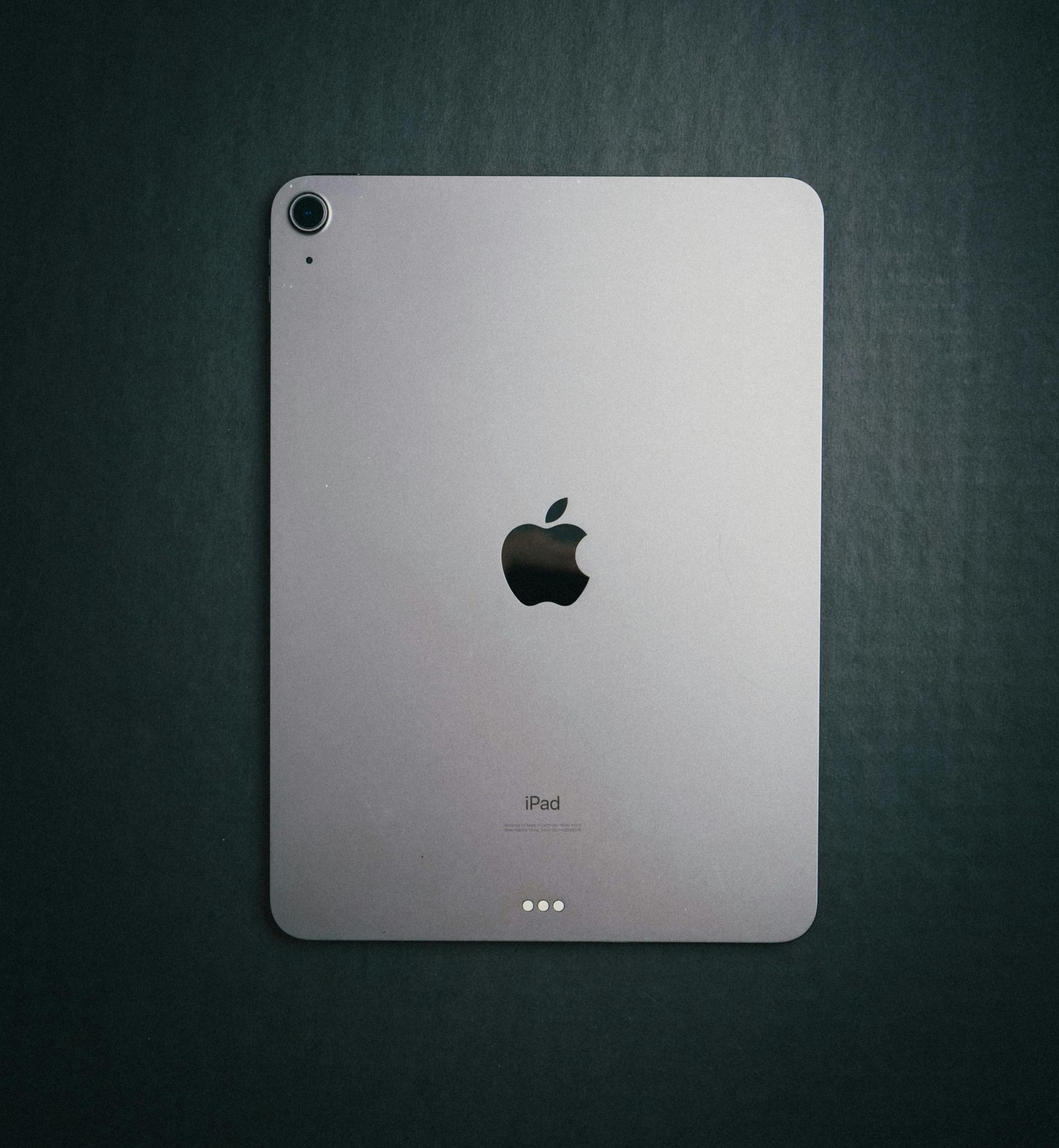 Silver Apple iPad on a dark textured surface, shown from the back with the Apple logo centered.