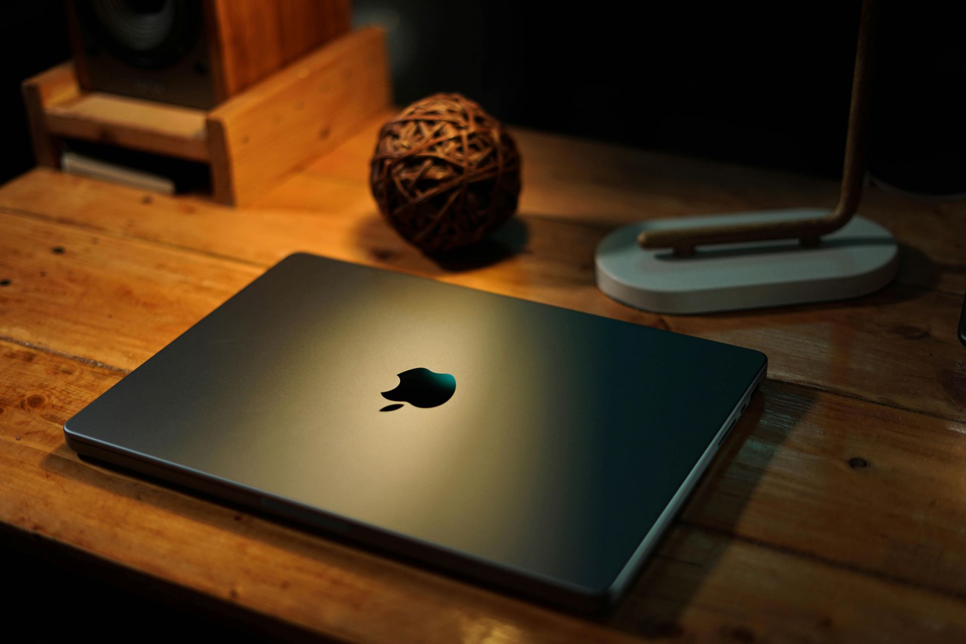 Closed MacBook on a wooden desk with warm lighting and a small decorative orb in the background