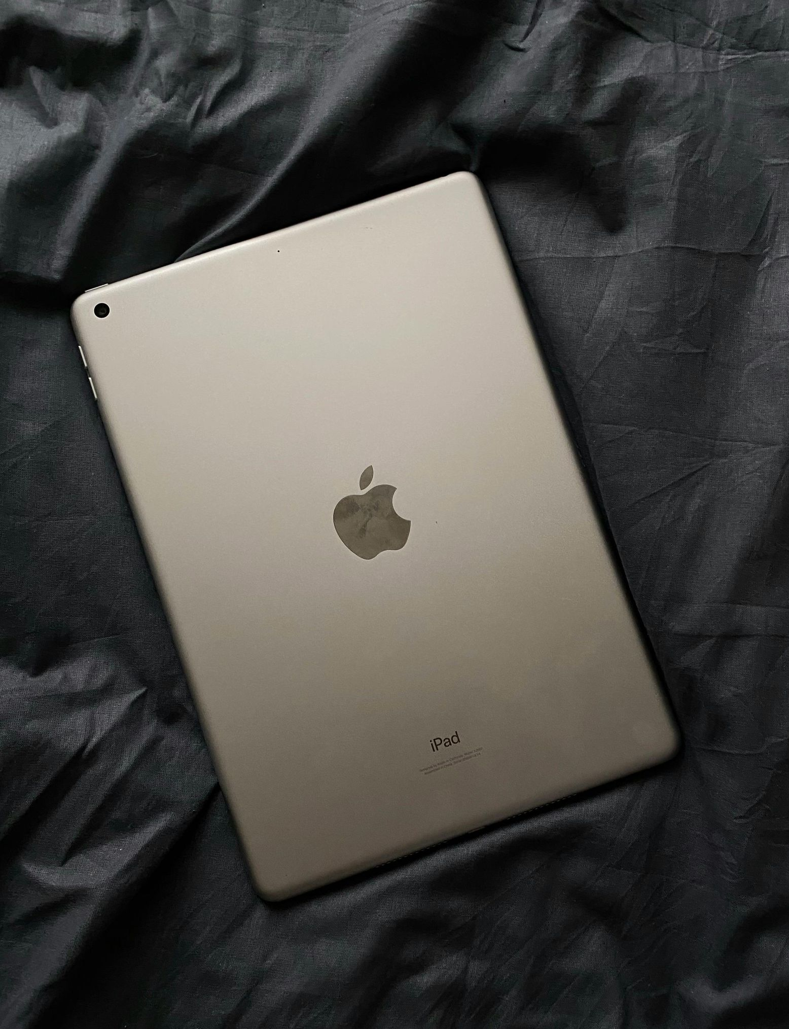 Silver Apple iPad lying on dark fabric, back side visible